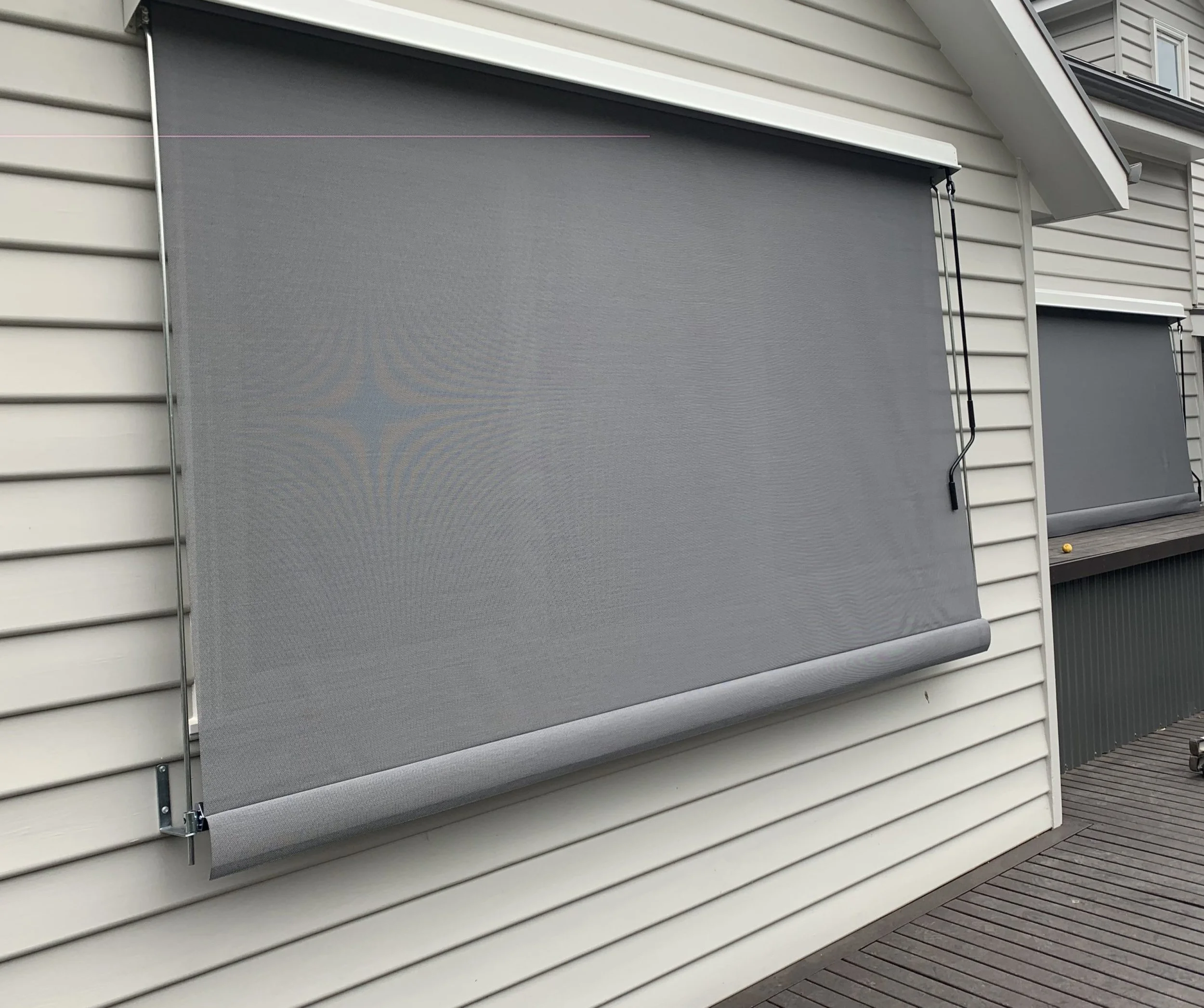 Image of a house exterior with gray roller blinds installed outside the windows, on a wooden deck.