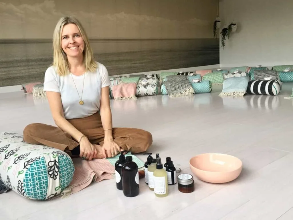 Rasasara founder Sonia Lloyd seated among skincare products, bowls and patterned floor cushions.