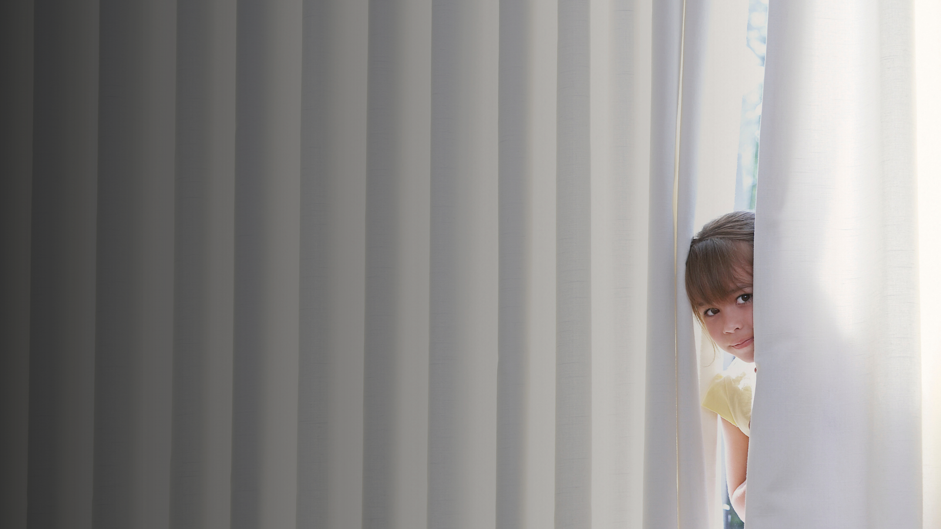 Child peeking through white curtains in a family home, illustrating how to choose practical curtains and blinds.
