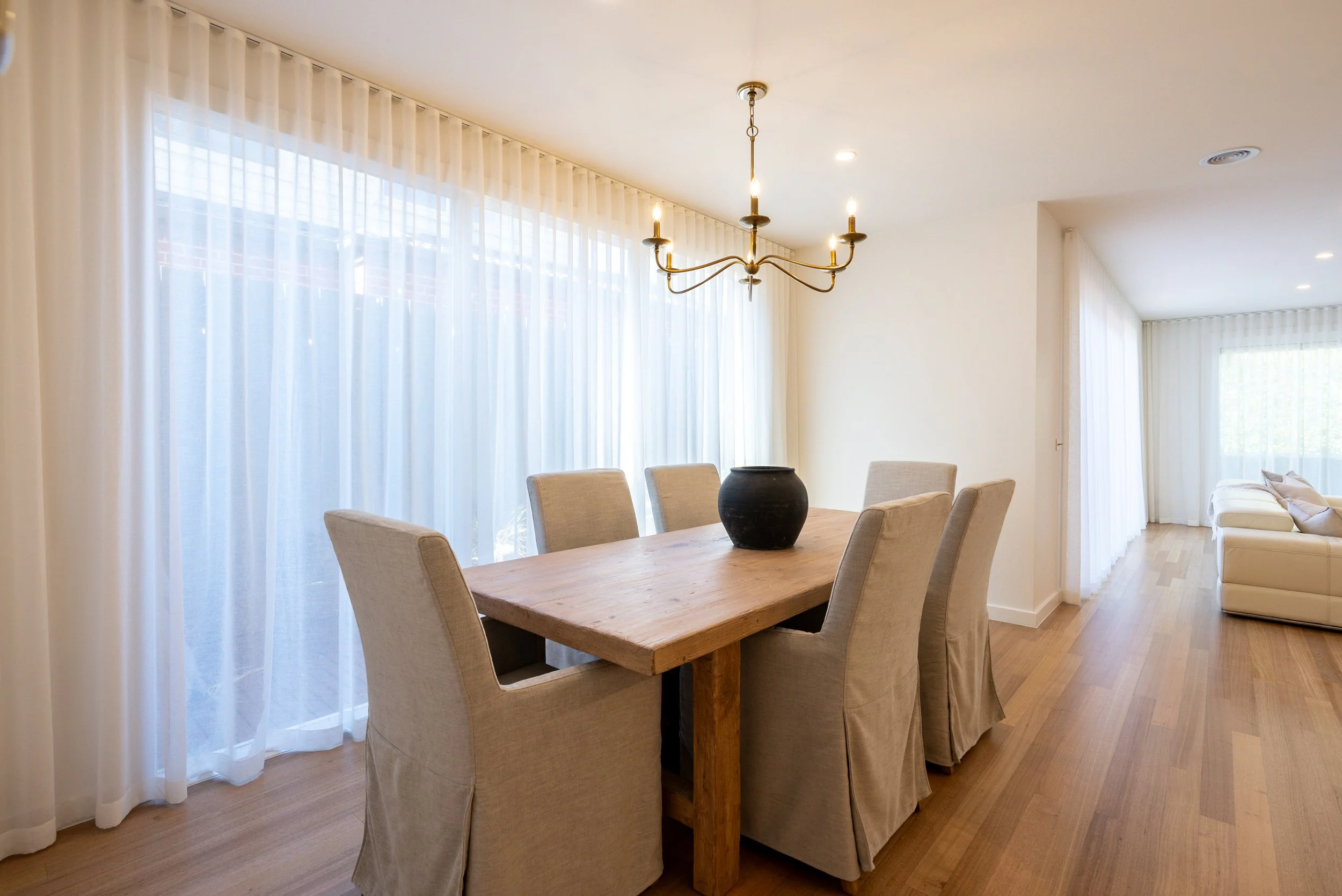 Floor-to-ceiling sheer curtains wrapping around a bright corner living room, installed by Evans Curtains and Blinds.