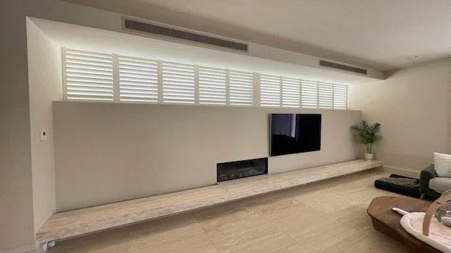 White plantation shutters by Evans Curtains and Blinds installed across high living room windows for privacy and light control.