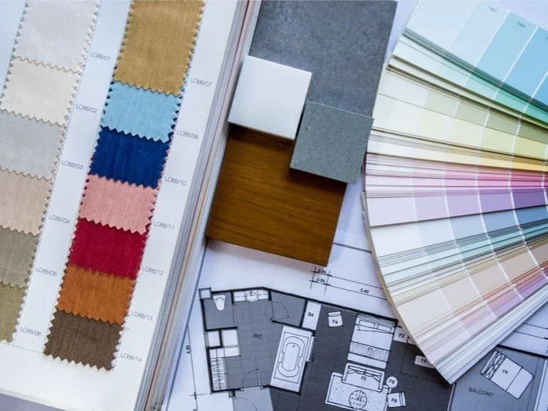 Collection of fabric swatches, color sample fan deck, small tile samples, wood and gray material samples, and part of a floor plan.