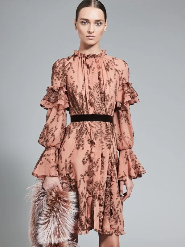 A woman in a pink dress with black abstract patterns, ruffled sleeves, and a black waist belt, holding a fur clutch.