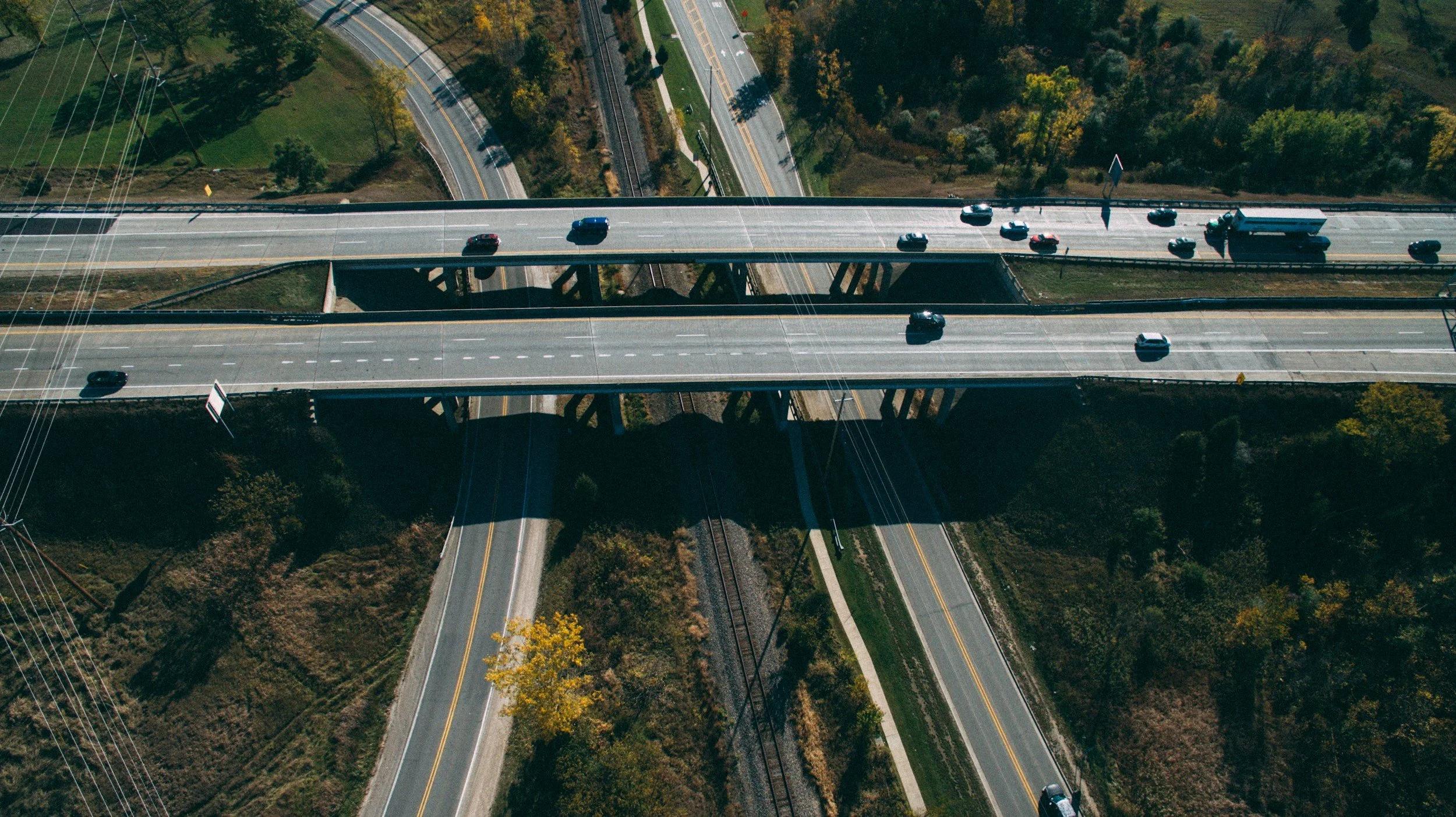 An aerial view of a highway overpass with cars traveling on it, and additional roads and greenery below.
