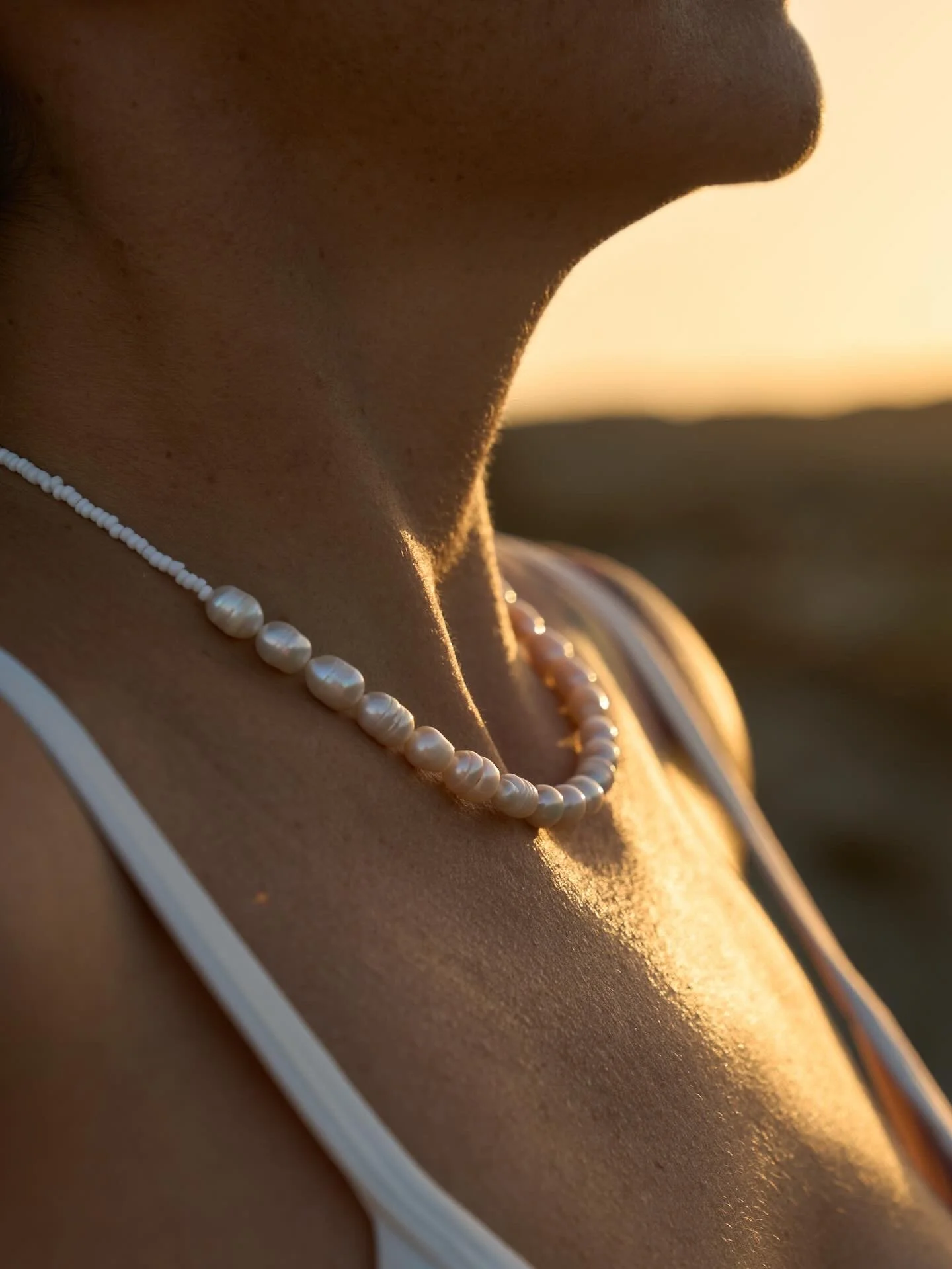 Close-up of a neck with a pearl necklace in warm sunset light.