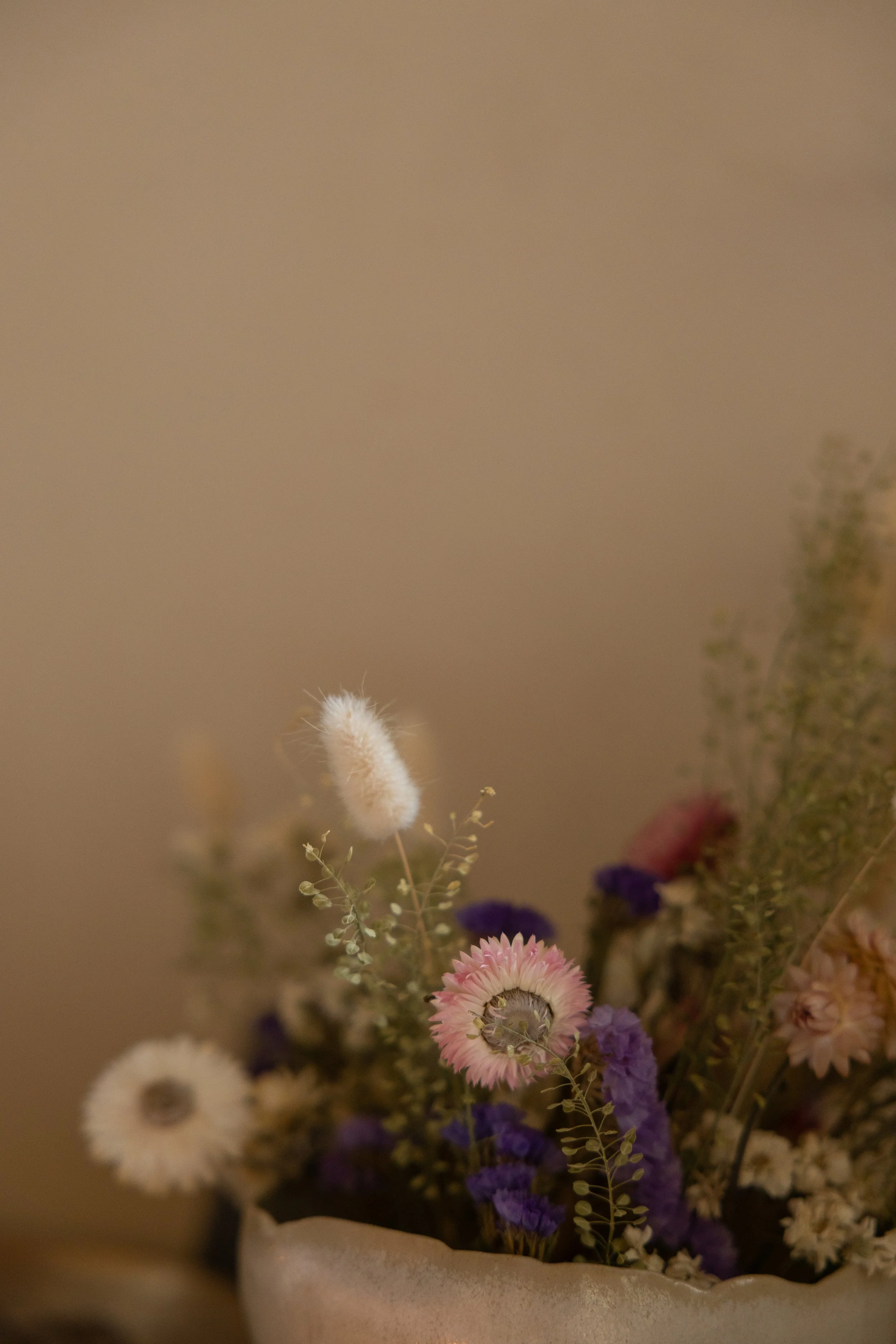 Blumenstrauß mit getrockneten Blumen in einer weißen Vase, Hintergrund beige.