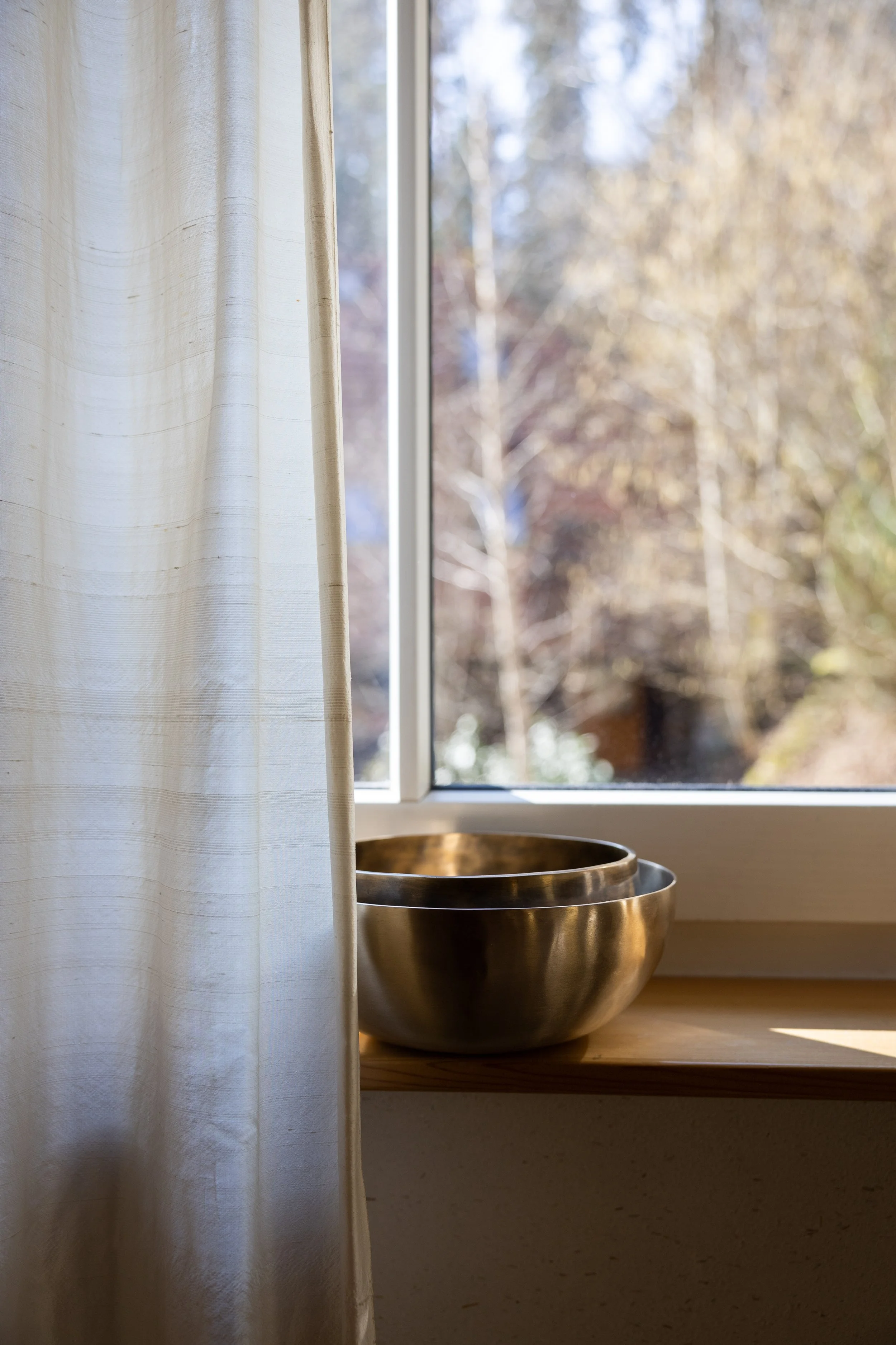 Zwei goldene Schalen auf einer Holzfensterbank vor einem offenen Fenster mit Blick auf Bäume im Freien, eine weiße Gardine an der linken Seite.