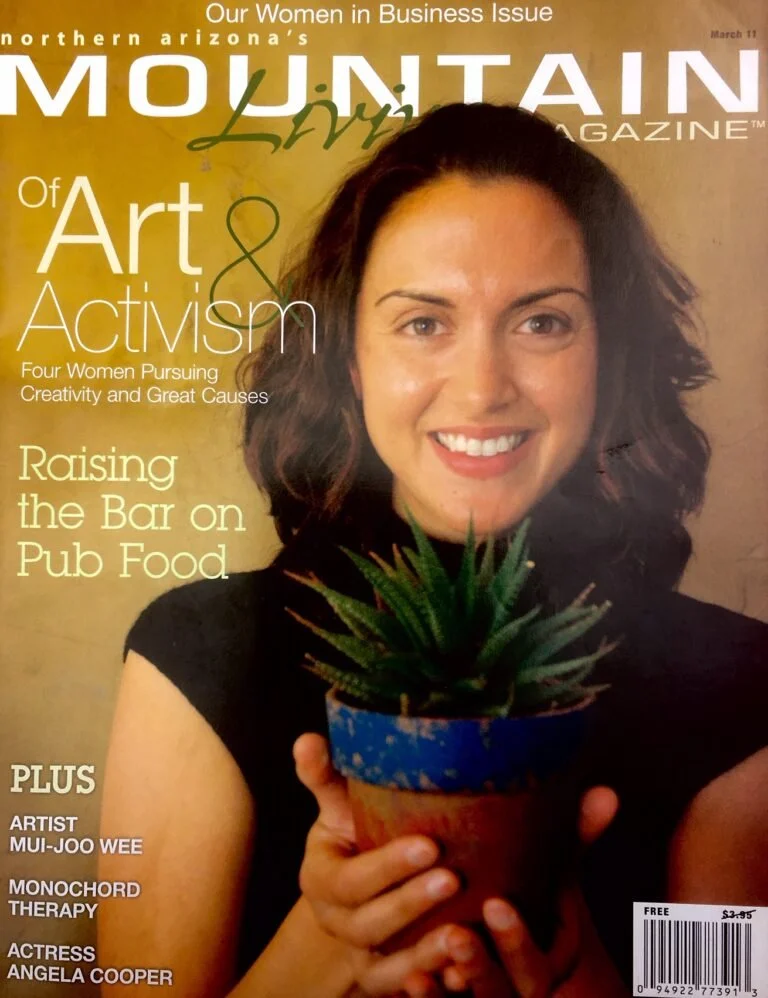 Cover of Mountain Living Magazine featuring a woman with dark curly hair in a black top, smiling and holding a potted succulent plant in a blue and orange pot. The magazine highlights art, activism, and women in business.