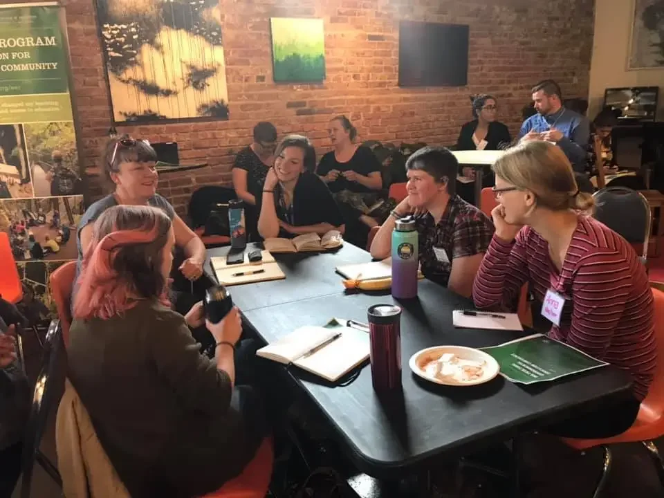 Group of people sitting around a table engaged in conversation at a casual indoor setting.