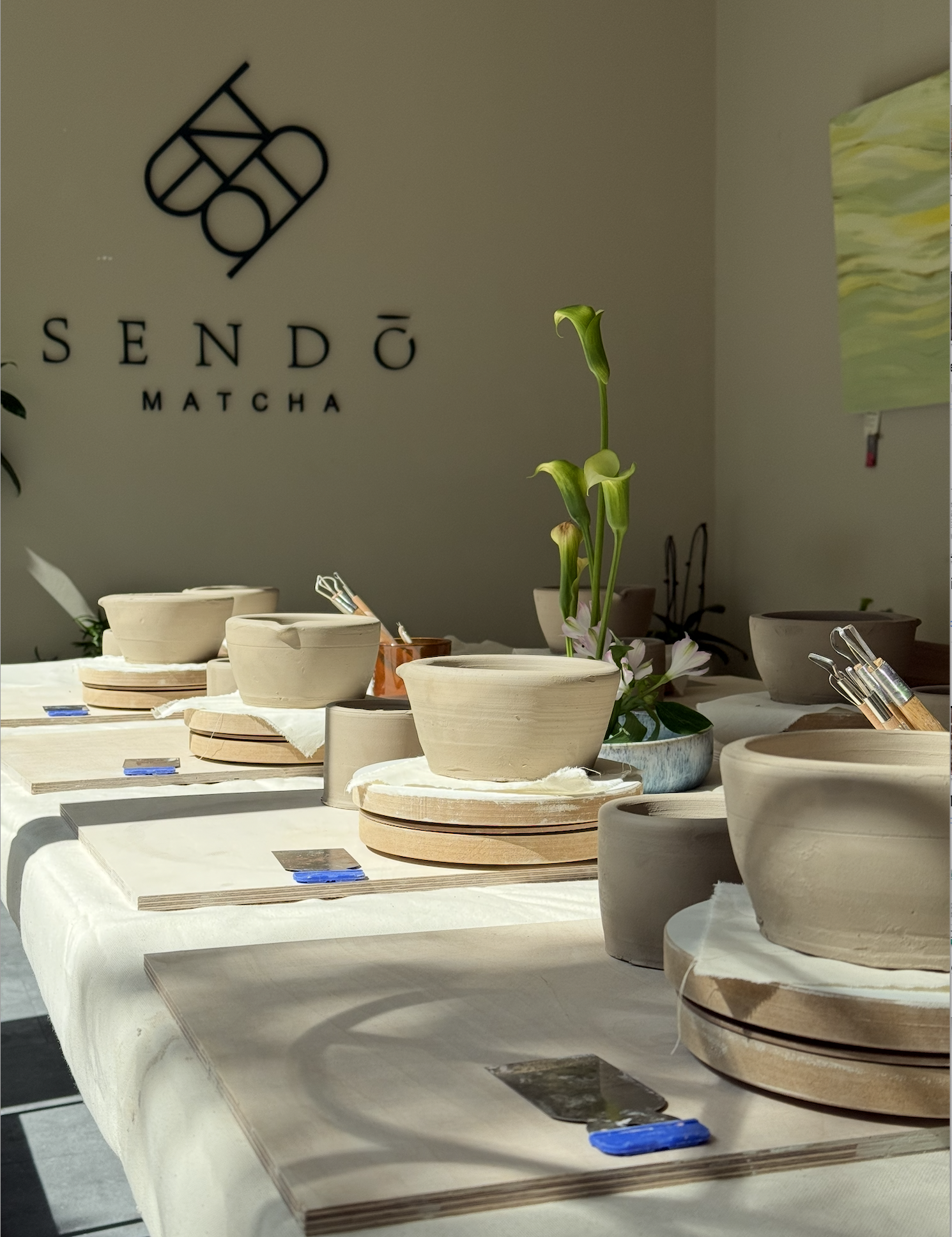 1. Für einen Keramik-Workshop vorbereiteter Tisch bei Sendo Matcha mit Chawans, Werkzeugen und Arbeitsplätzen im Sonnenlicht.