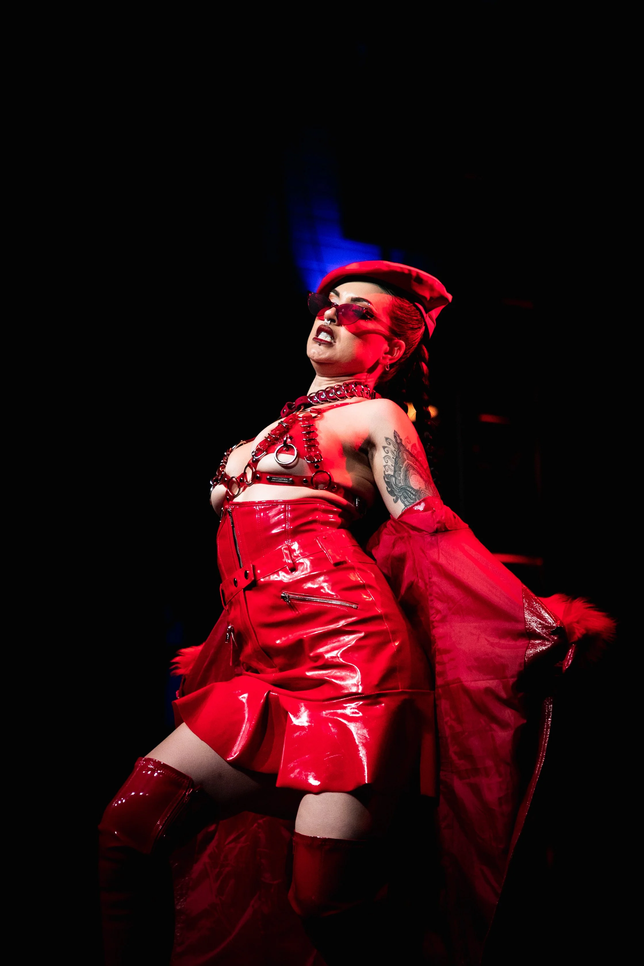 A woman dressed in red, wearing sunglasses, a beret, and jewelry, performing on stage against a dark background.