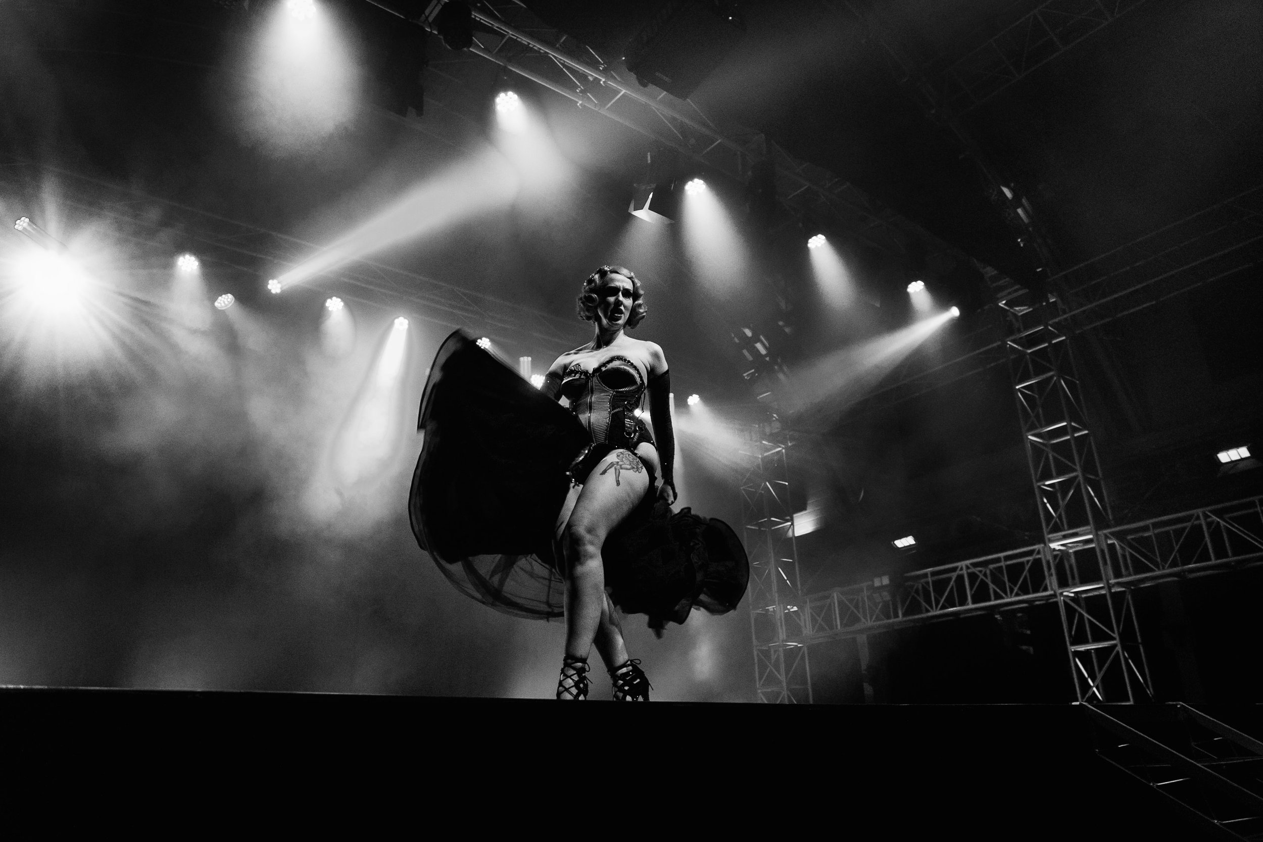A performer on stage dressed in vintage lingerie and high heels, illuminated by spotlights in a black and white photo.