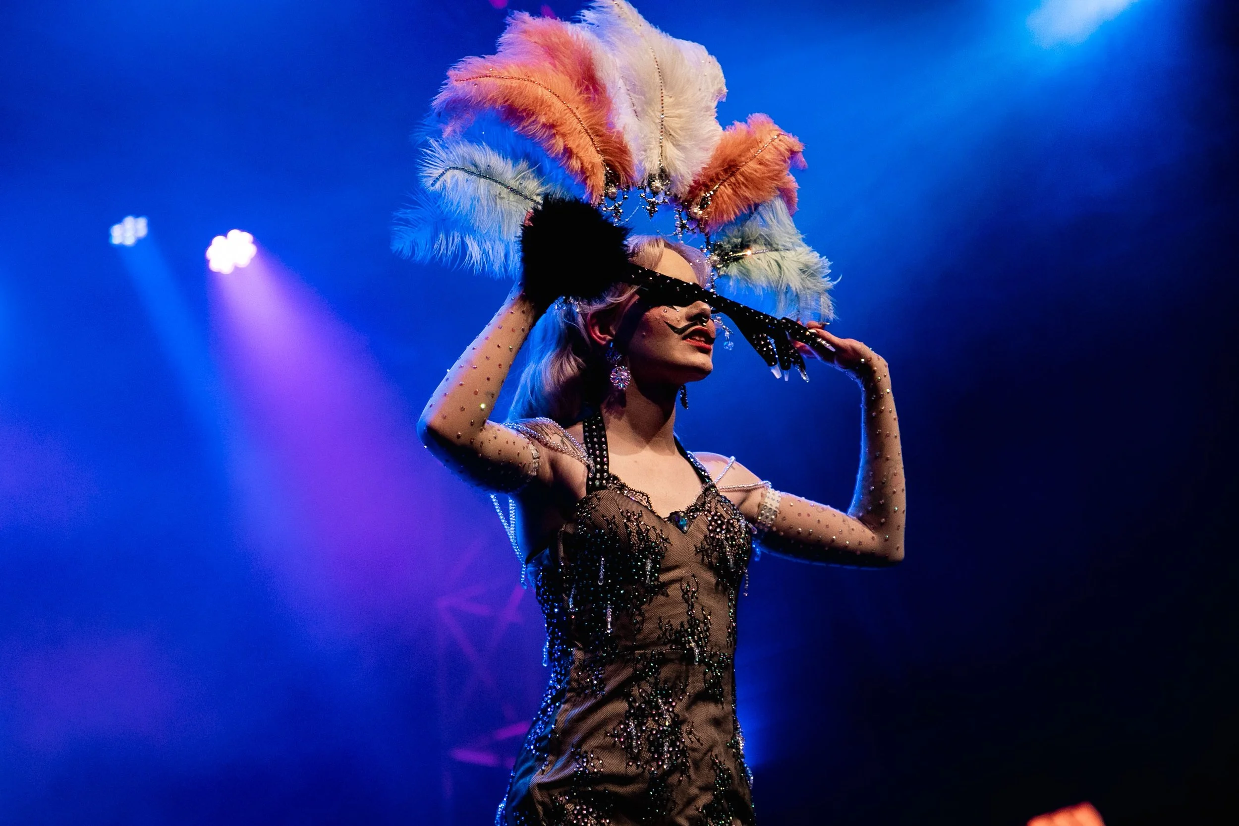 Performer in a costume posing on stage with a large feather headdress.