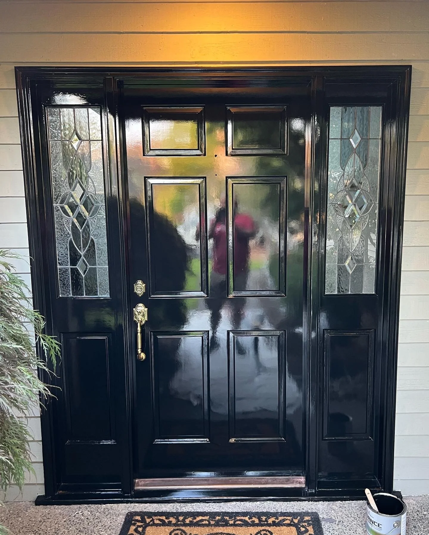 Black front door with decorative glass side panels, a gold door handle, and a doormat in front.