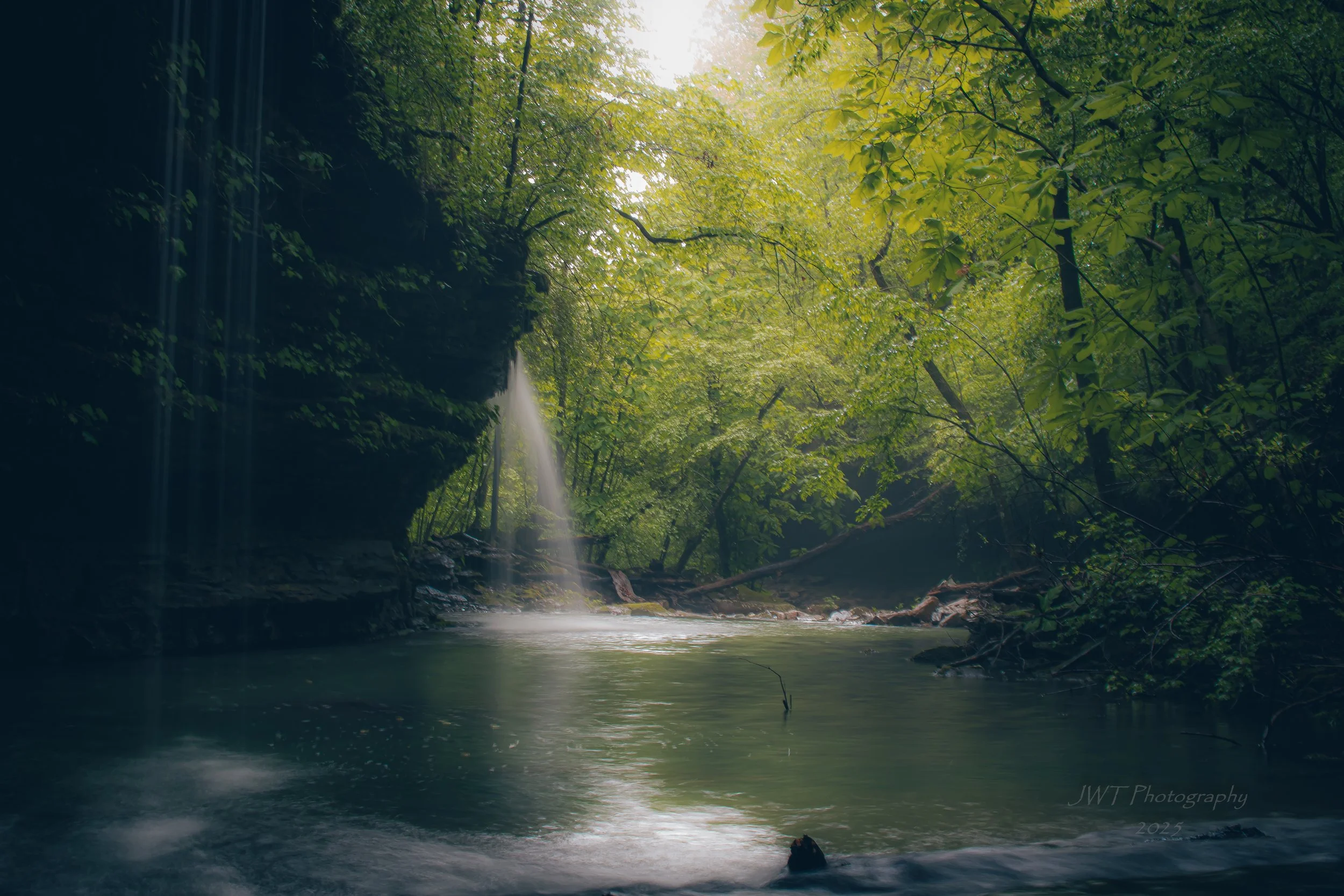 A serene forest scene with a waterfall cascading over rocks into a calm river, surrounded by lush green trees with sunlight filtering through the canopy.