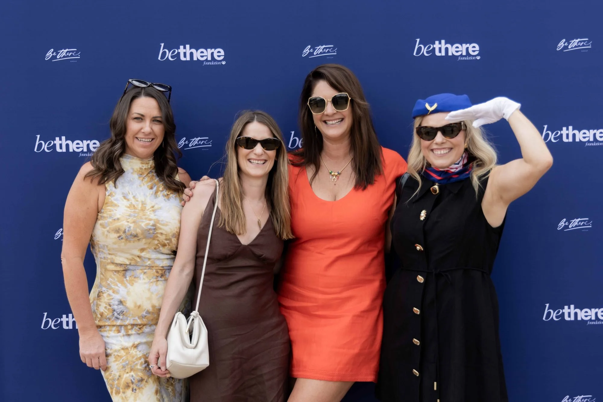 Four guests striking a playful pose at the Be There Foundation media wall at The Rolling Lunch 2026