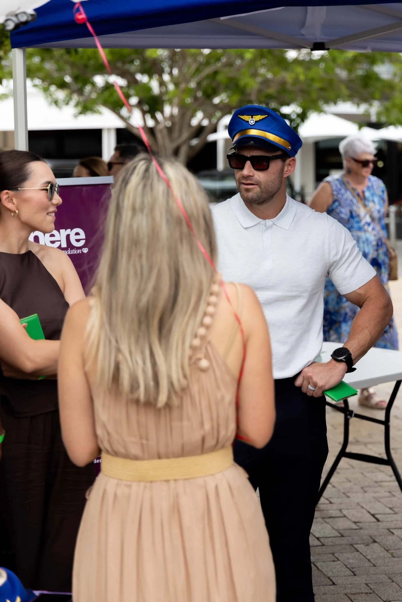 Guests chatting under the marquee at The Rolling Lunch 2026, one wearing a pilot's cap for the Around the World theme
