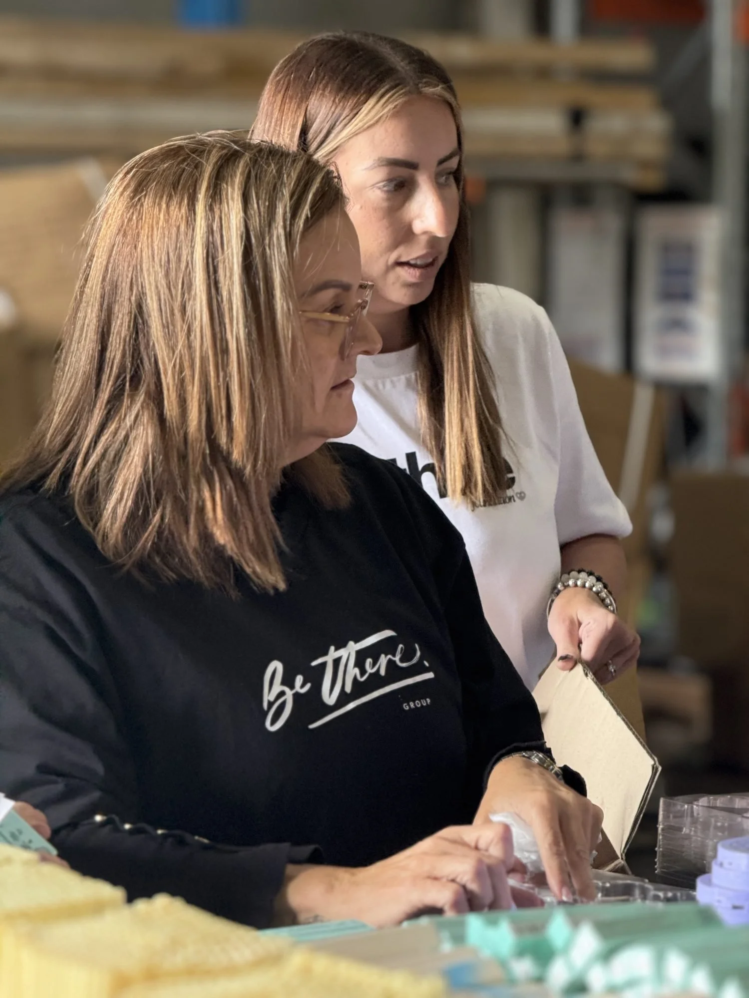 Two volunteers in Be There shirts packing items together
