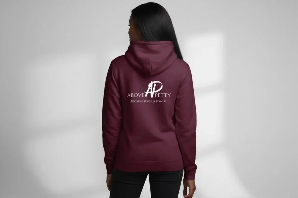 Back view of a woman wearing a maroon hoodie with a design and text on the back that says 'Above AD PettY because peace is power'