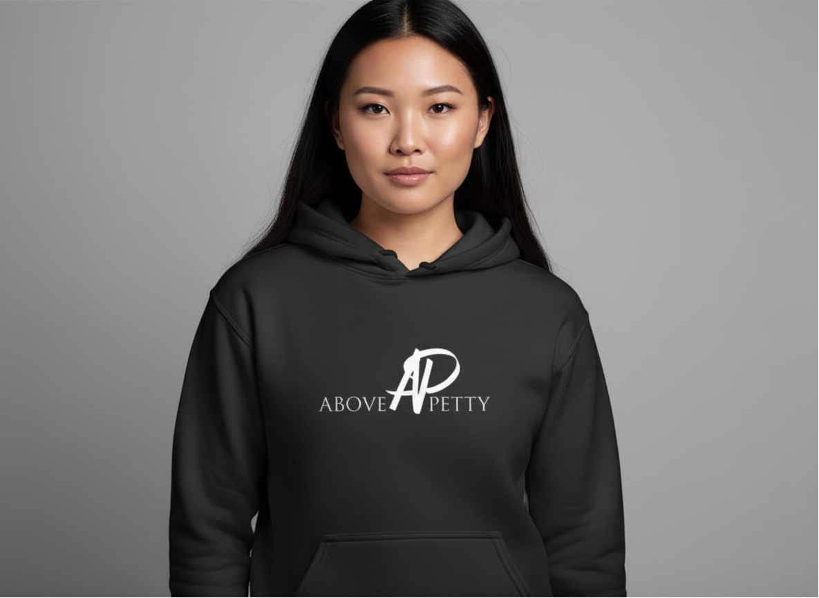 A woman with long black hair wearing a black hoodie with the words 'Above Petty' and a stylized 'AP' logo on the front, standing against a plain gray background.