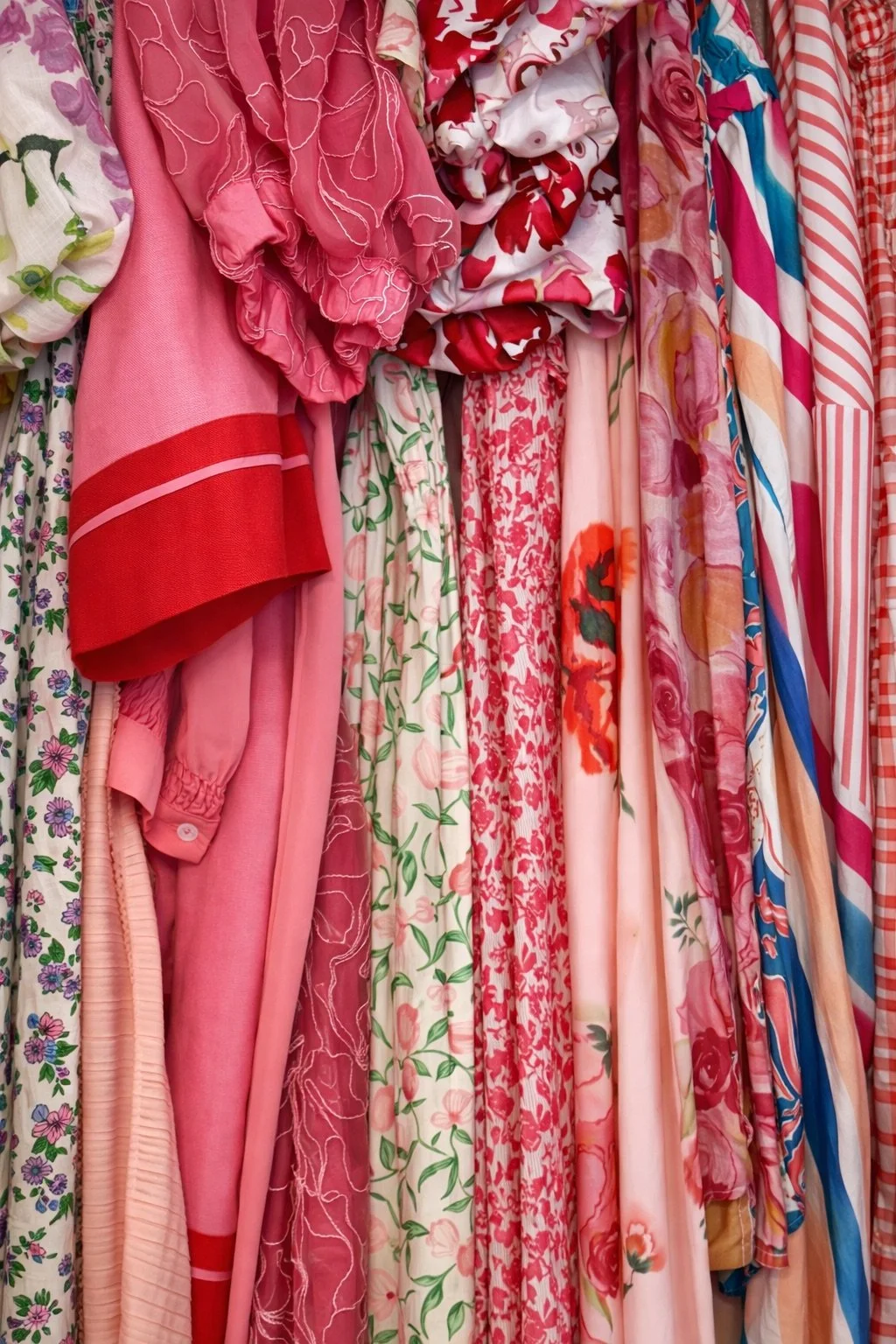 A collection of pink, red, and multicolored floral and patterned dresses hanging on a clothing rack.
