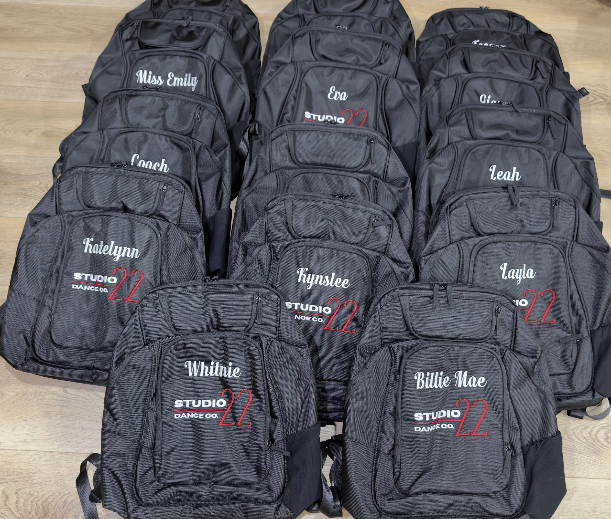 black backpacks with embroidered company logo and name on the front pocket, displayed on a wooden background