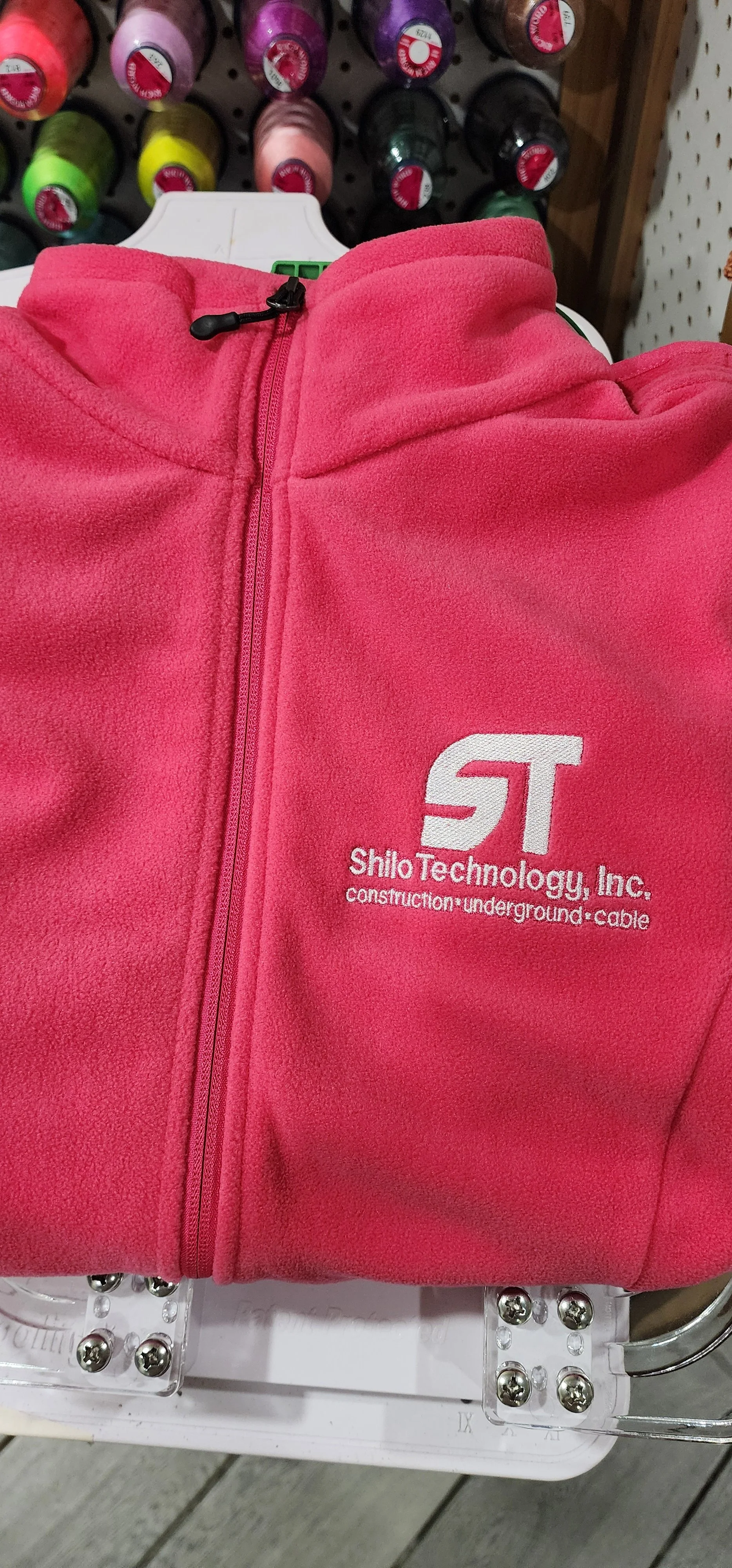 Pink fleece jacket with a black zipper pull, displaying the logo and text 'Shilo Technology, Inc. construction underground cable' embroidered on the front.