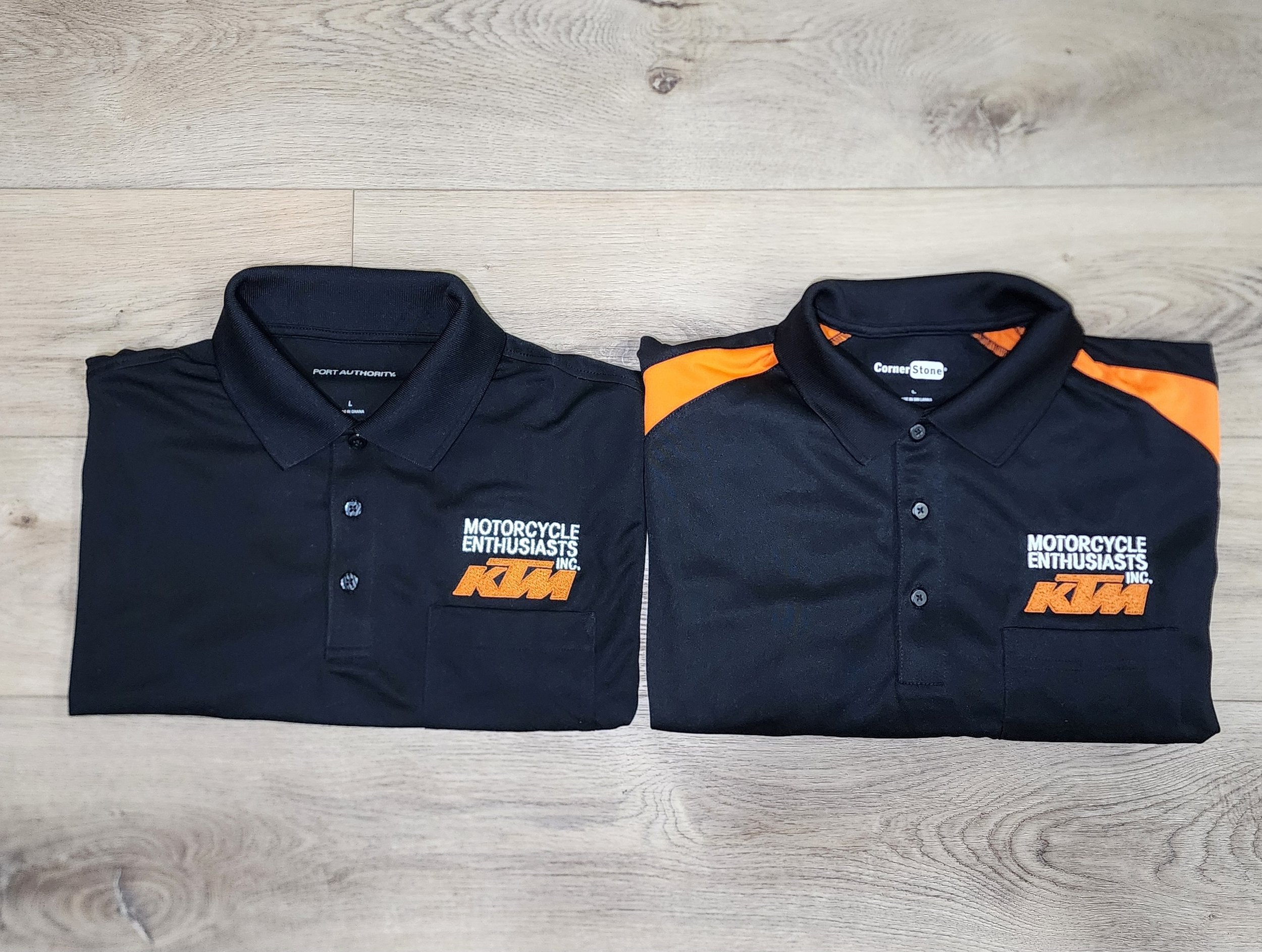 Two folded black polo shirts with KTM motorcycle logo and text, one with orange shoulder accents.