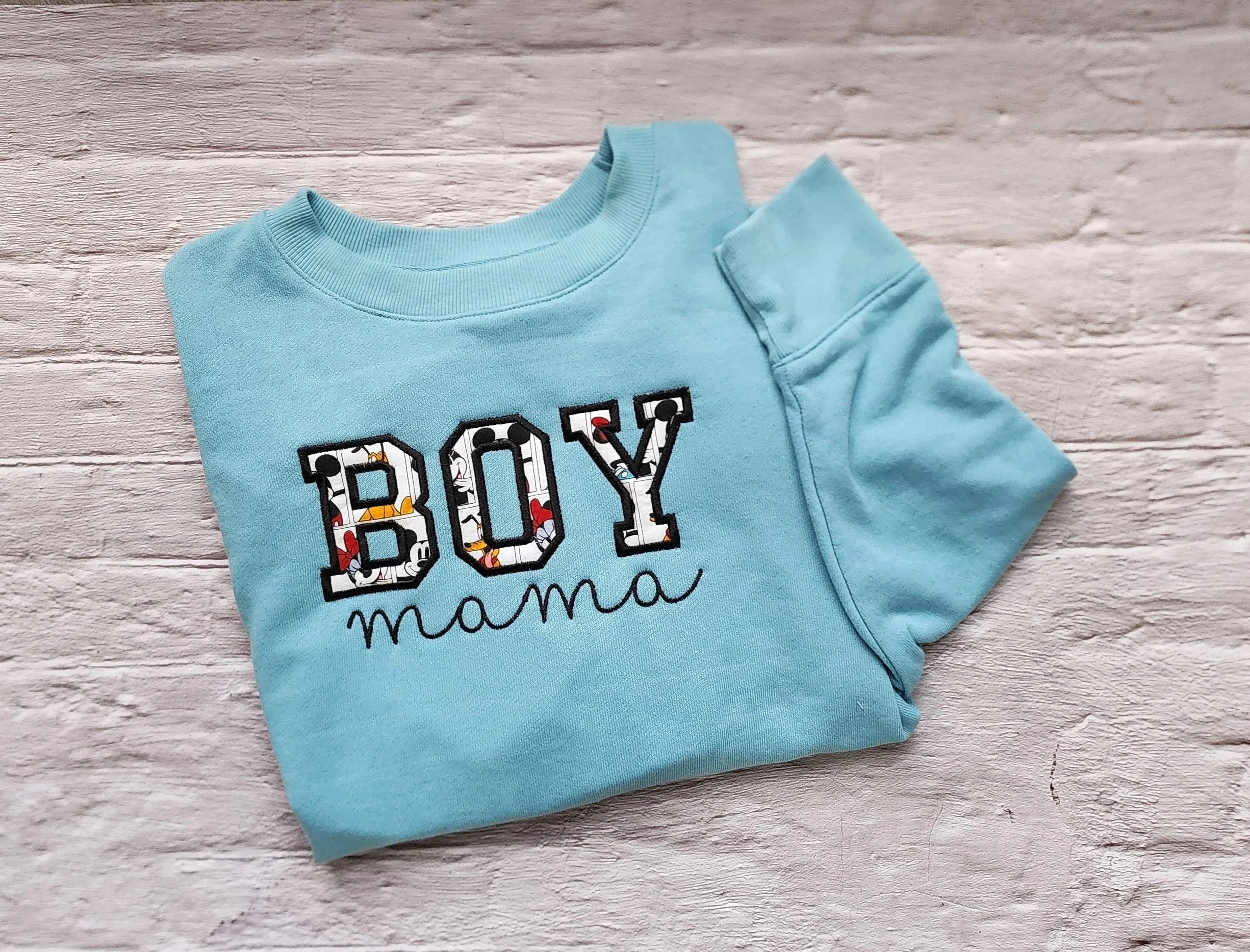 folded light blue crewneck with embroidered design saying boy mama