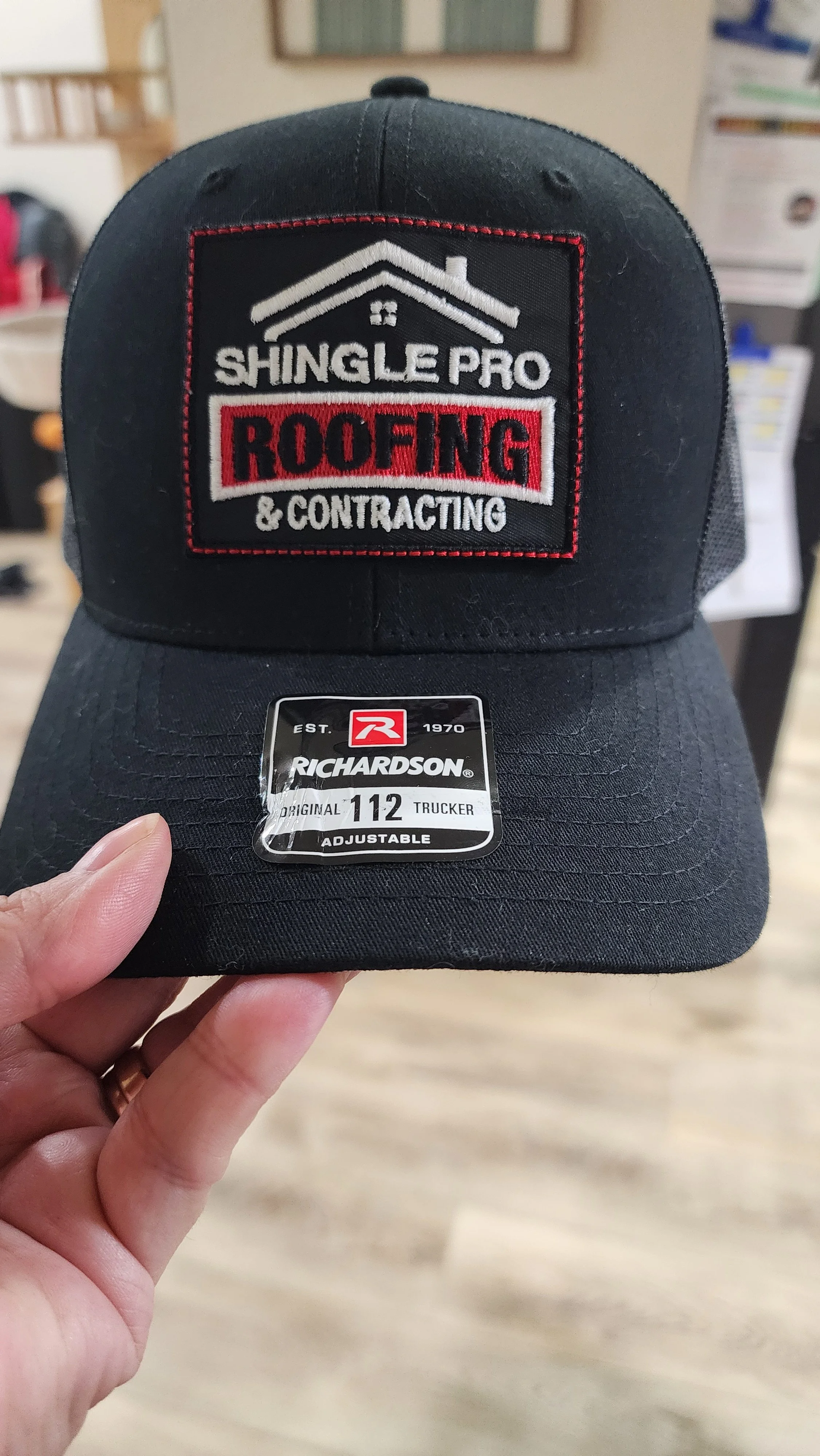 Black Richardson trucker cap with 'Shingle Pro Roofing & Contracting' embroidered patch on the front.