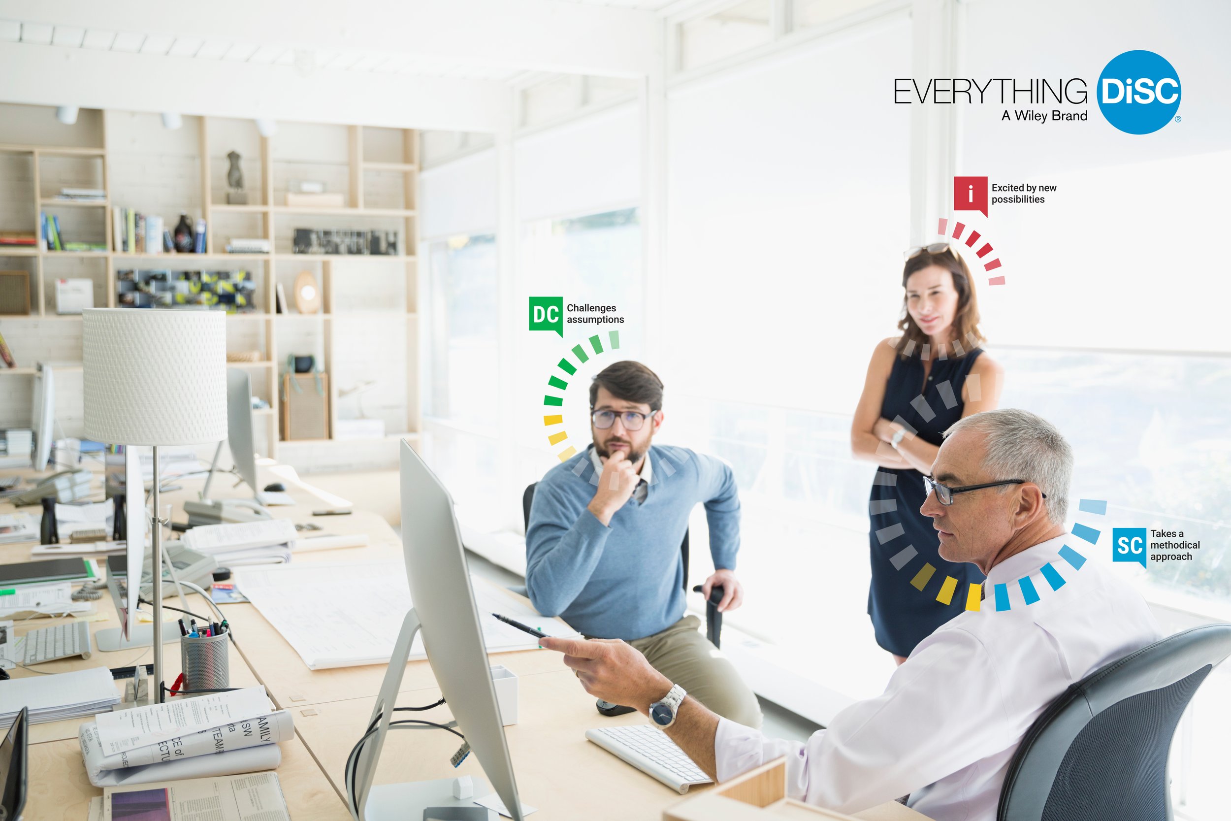 Three people in a modern office with large windows, engaging in a discussion. The man on the right, with gray hair and glasses, is pointing at a computer screen. The man in the middle, with dark hair and a beard, is sitting and resting his chin on his hand, looking at the man on the right. The woman on the left, with shoulder-length hair, is standing with arms crossed, smiling. The image contains various colored labels with text: green label reading 'DC Challenges assumptions,' red label reading 'i Excited by new possibilities,' and blue label reading 'SC Takes a methodical approach.' The office has a wooden desk with papers, a lamp, and multiple computer monitors.