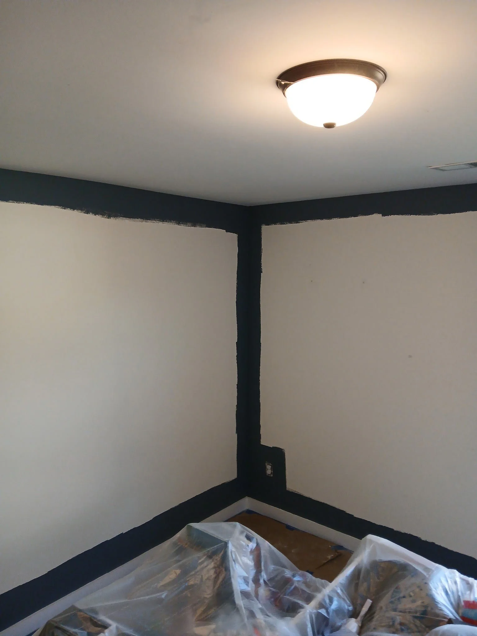 Corner of a room during painting renovation with dark trim and a plastic-covered floor.