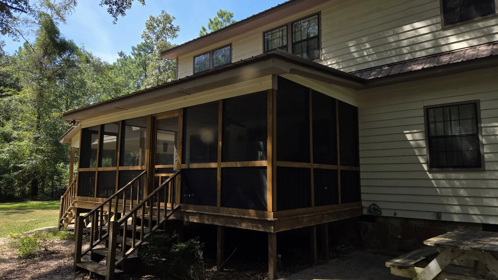 Back view of a house with a screened porch under construction, with wooden stairs leading up to it and surrounded by trees.