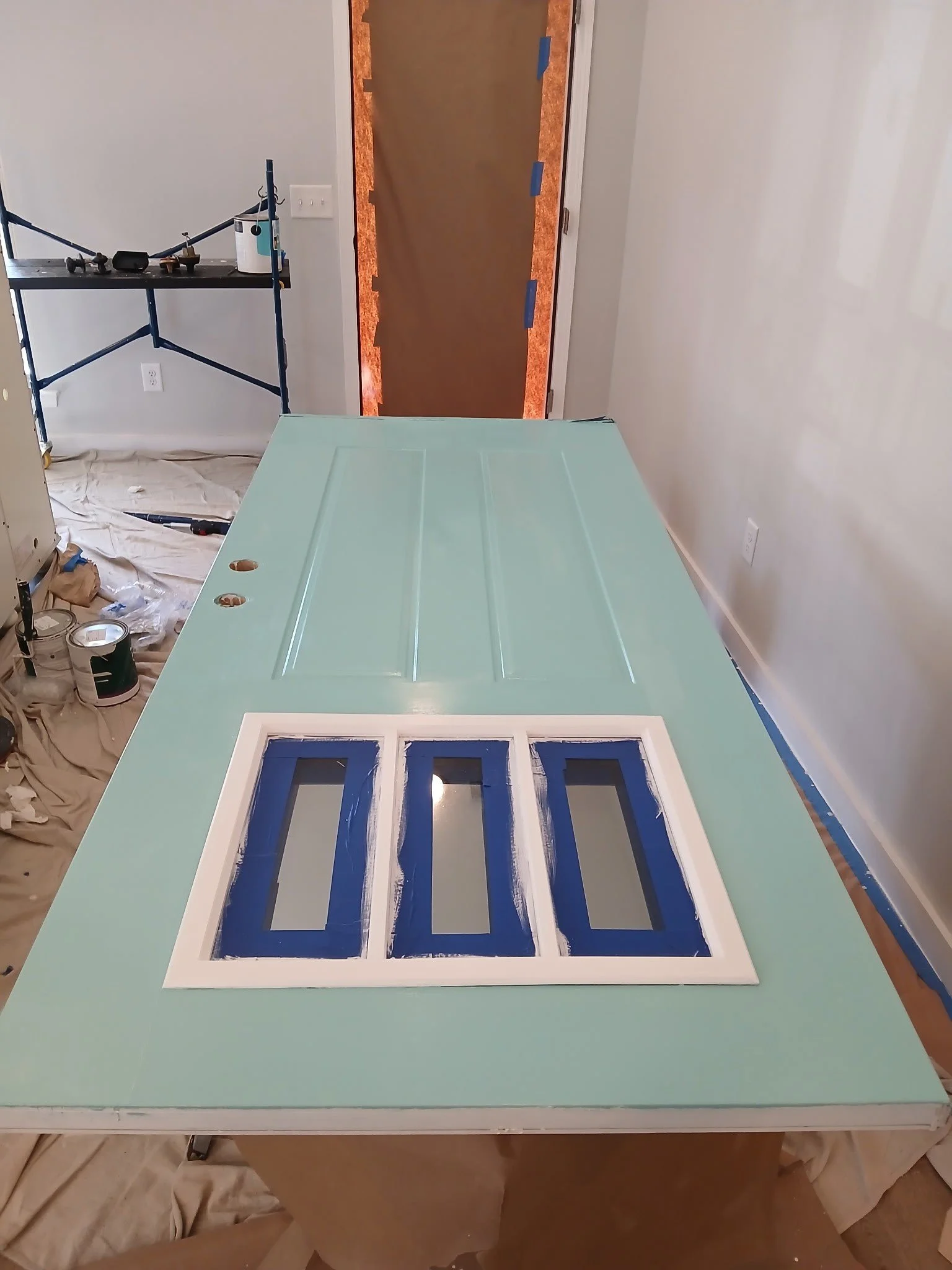 A mint green door lying on a work table in a room under renovation, with painting supplies and construction tools around.