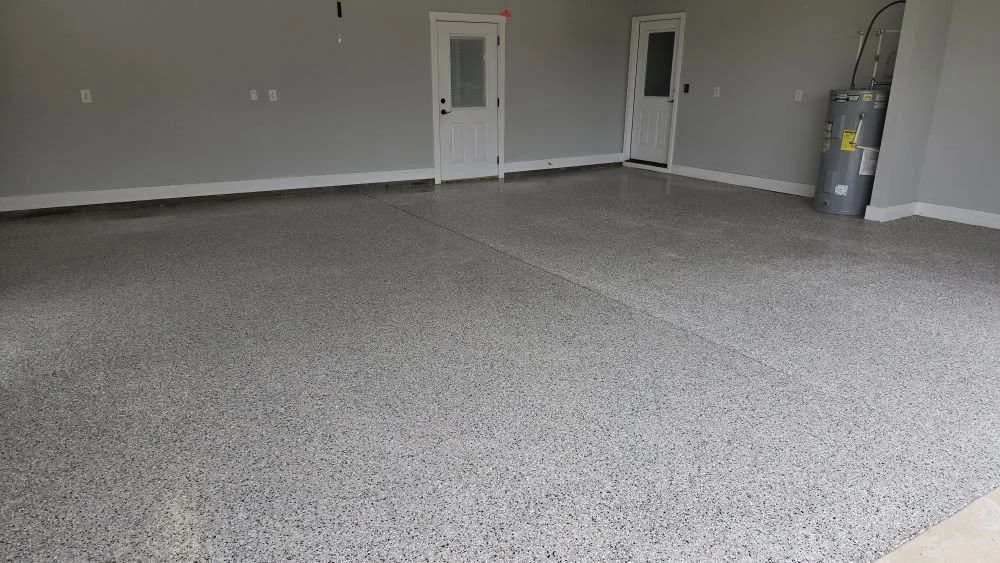 Empty garage with gray speckled epoxy floor, two white doors with windows, and a water heater in the corner.