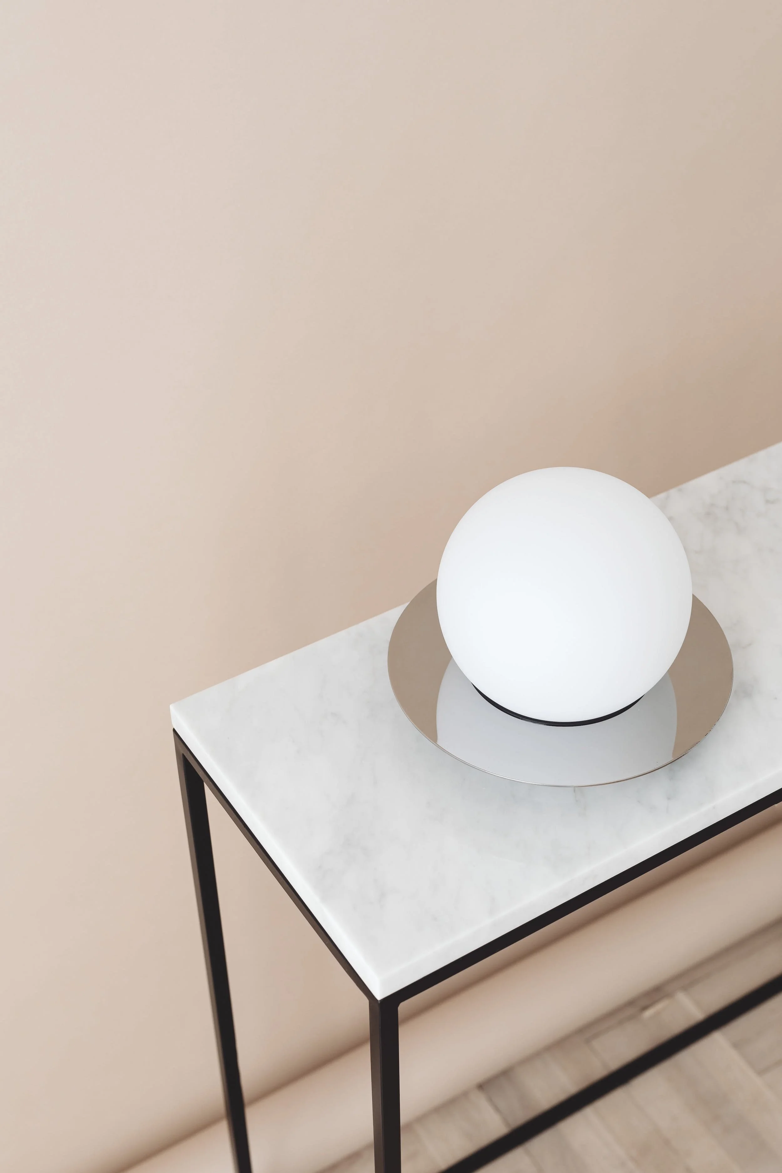 A modern table with a white marble top, black metal legs, and a spherical white lamp on a round metallic tray.
