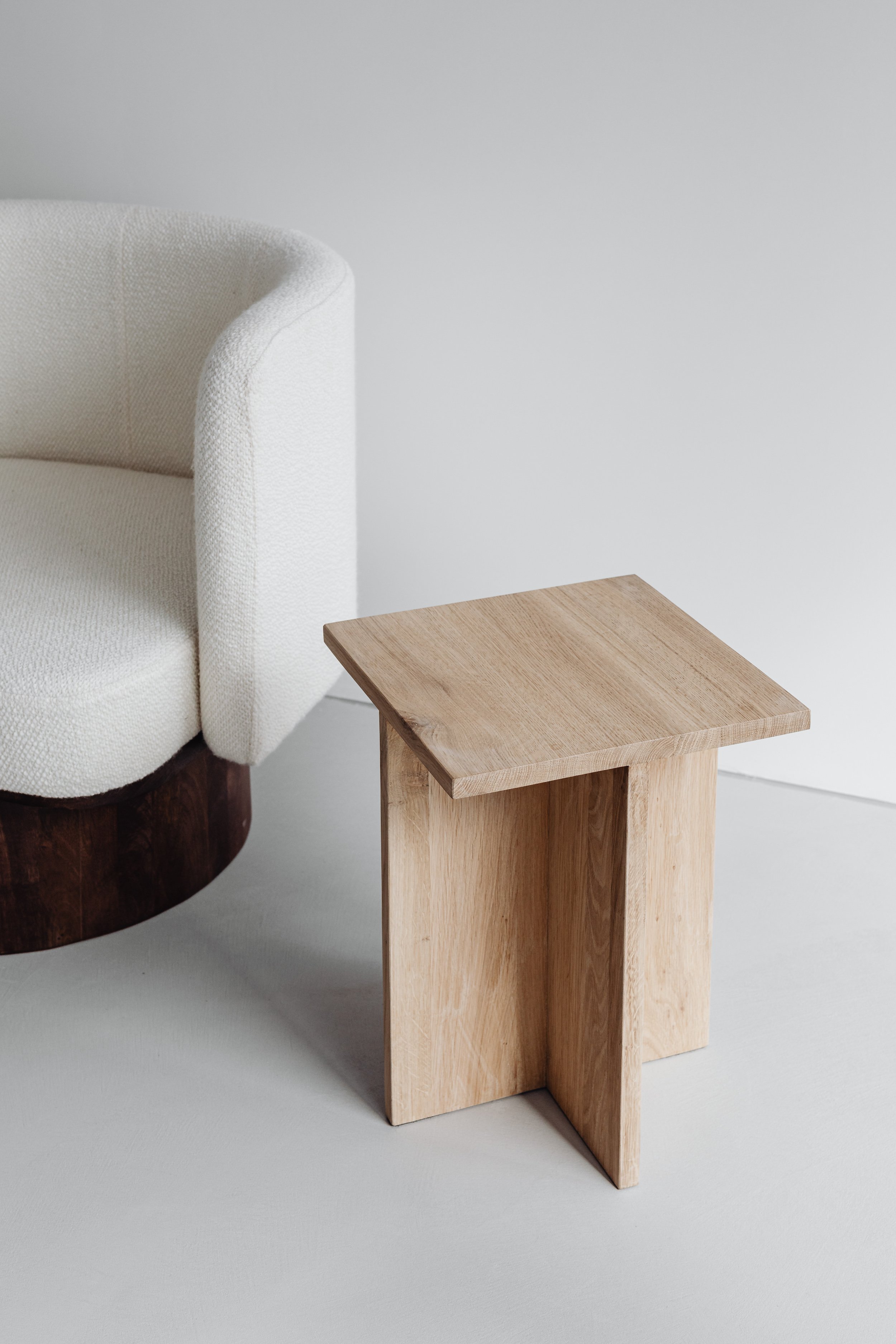A minimalist interior with a textured white armchair and a small wooden side table.