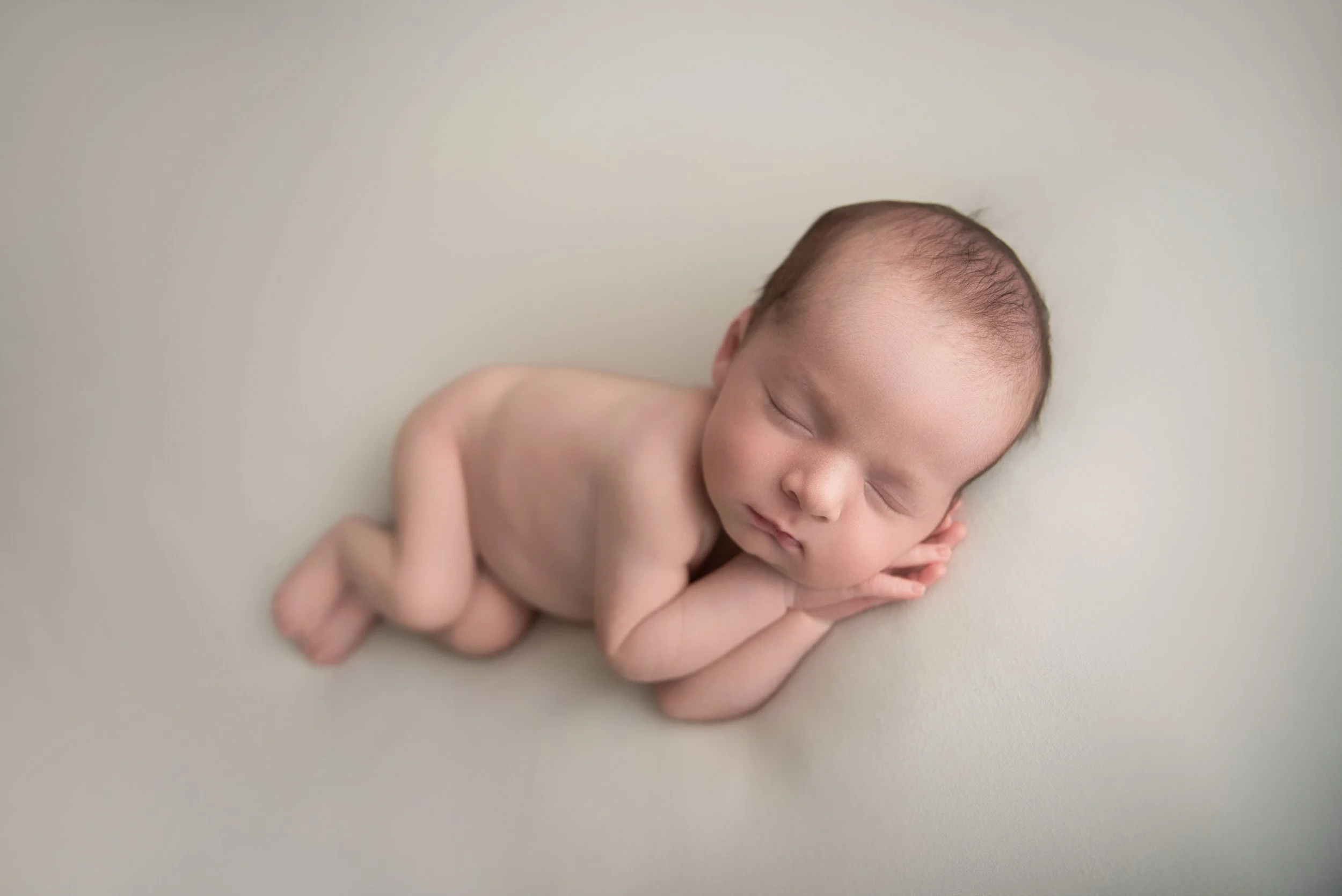 Close-up of a newborn baby sleeping on a soft surface with hands under cheek and eyes closed.