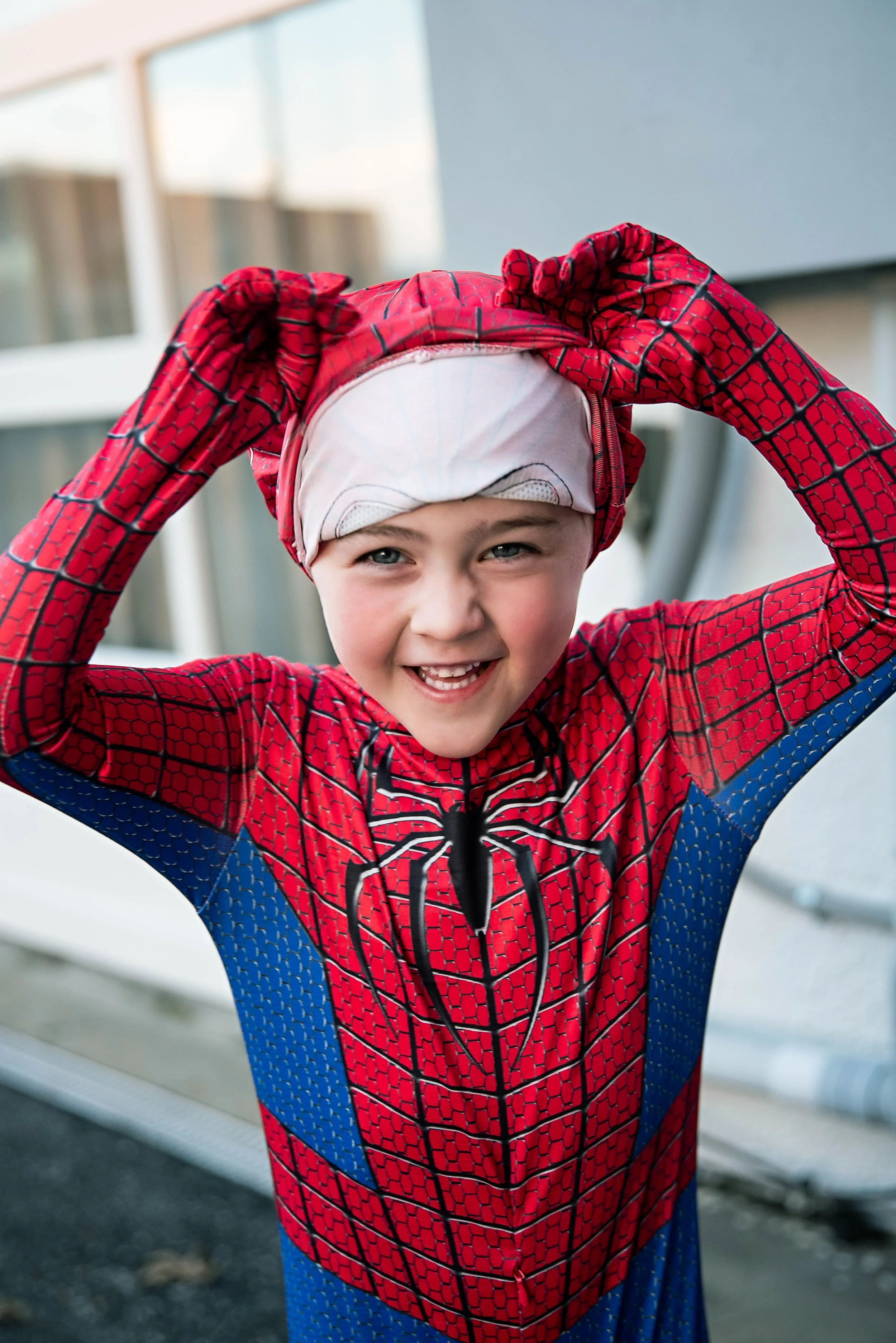 Young boy dressed as Spider-Man smiling and adjusting his costume outdoors