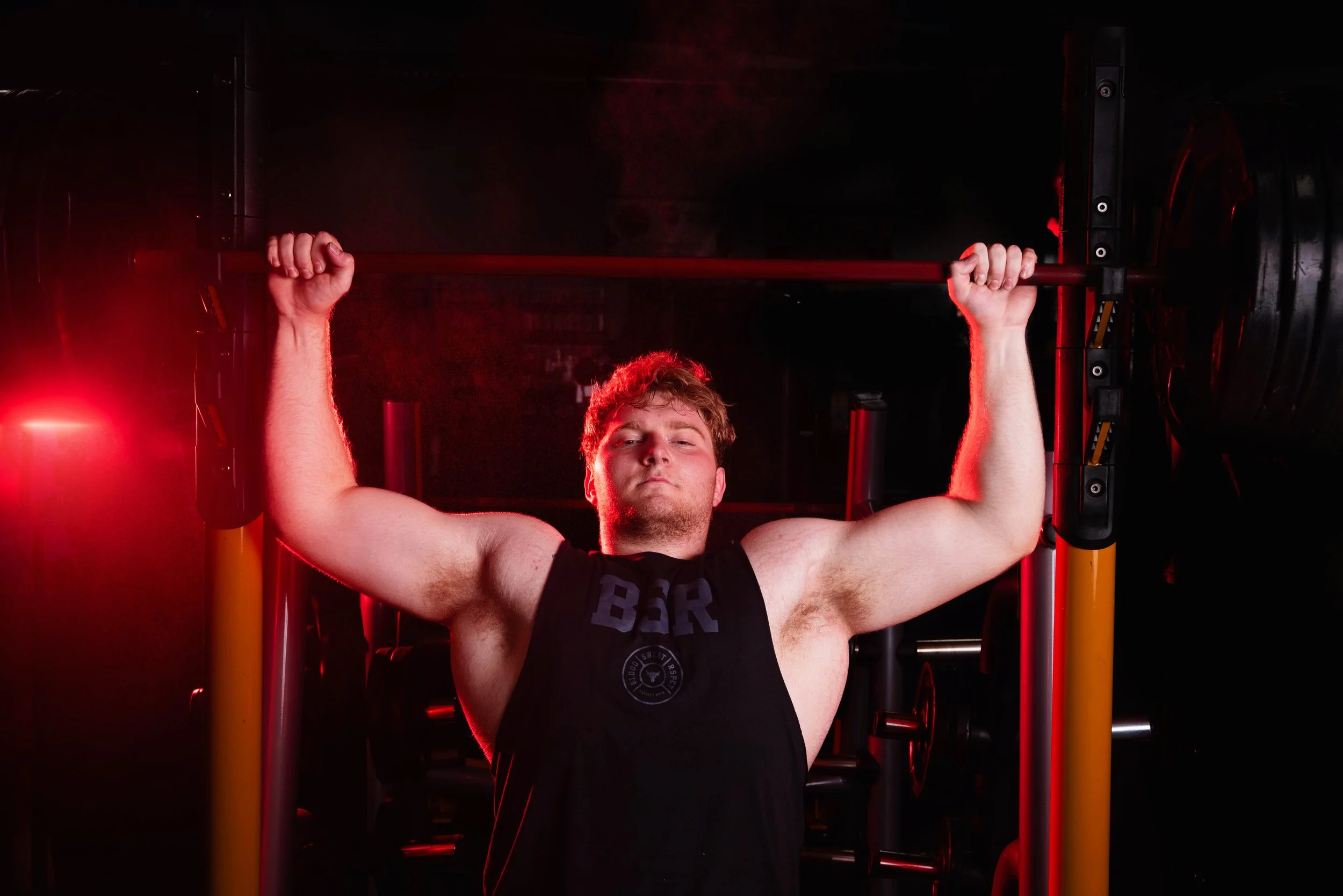 Young man lifting a barbell in a dark gym with red lighting.