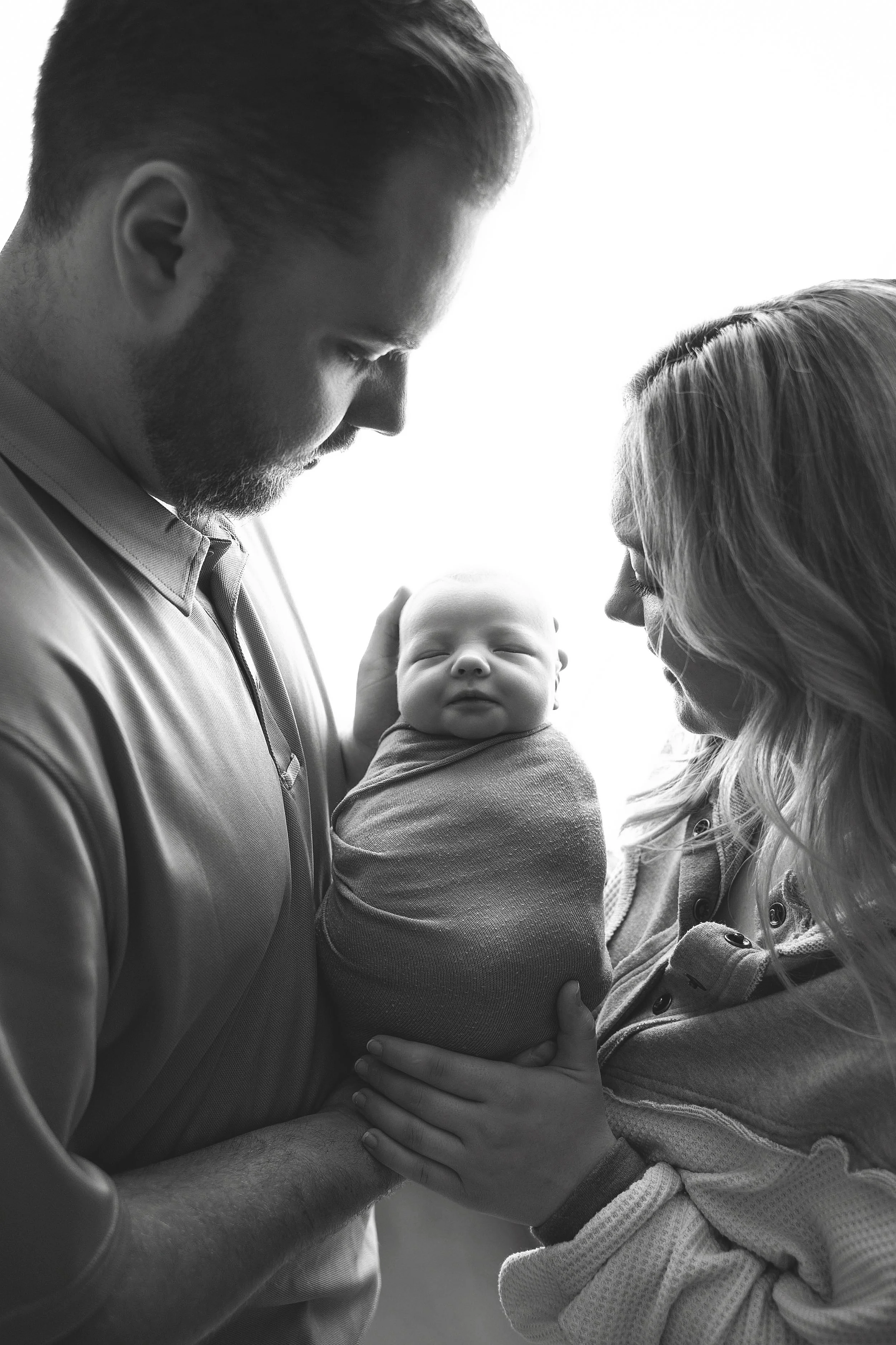 A black and white photo of a man and woman holding a baby between them, both looking at the baby with gentle expressions.