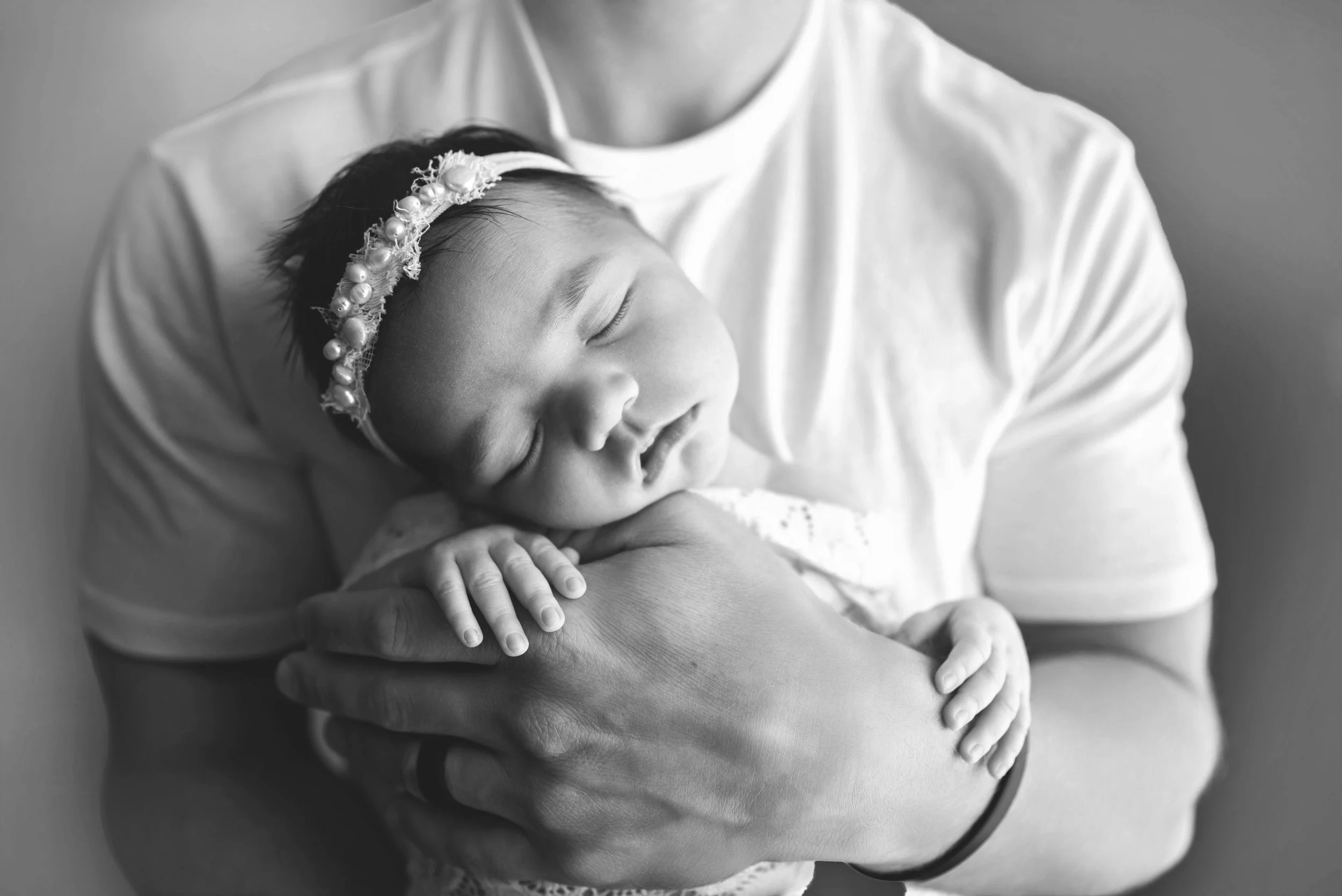 A young girl with a headband smiling and sleeping peacefully in an adult's arms, black and white photo.