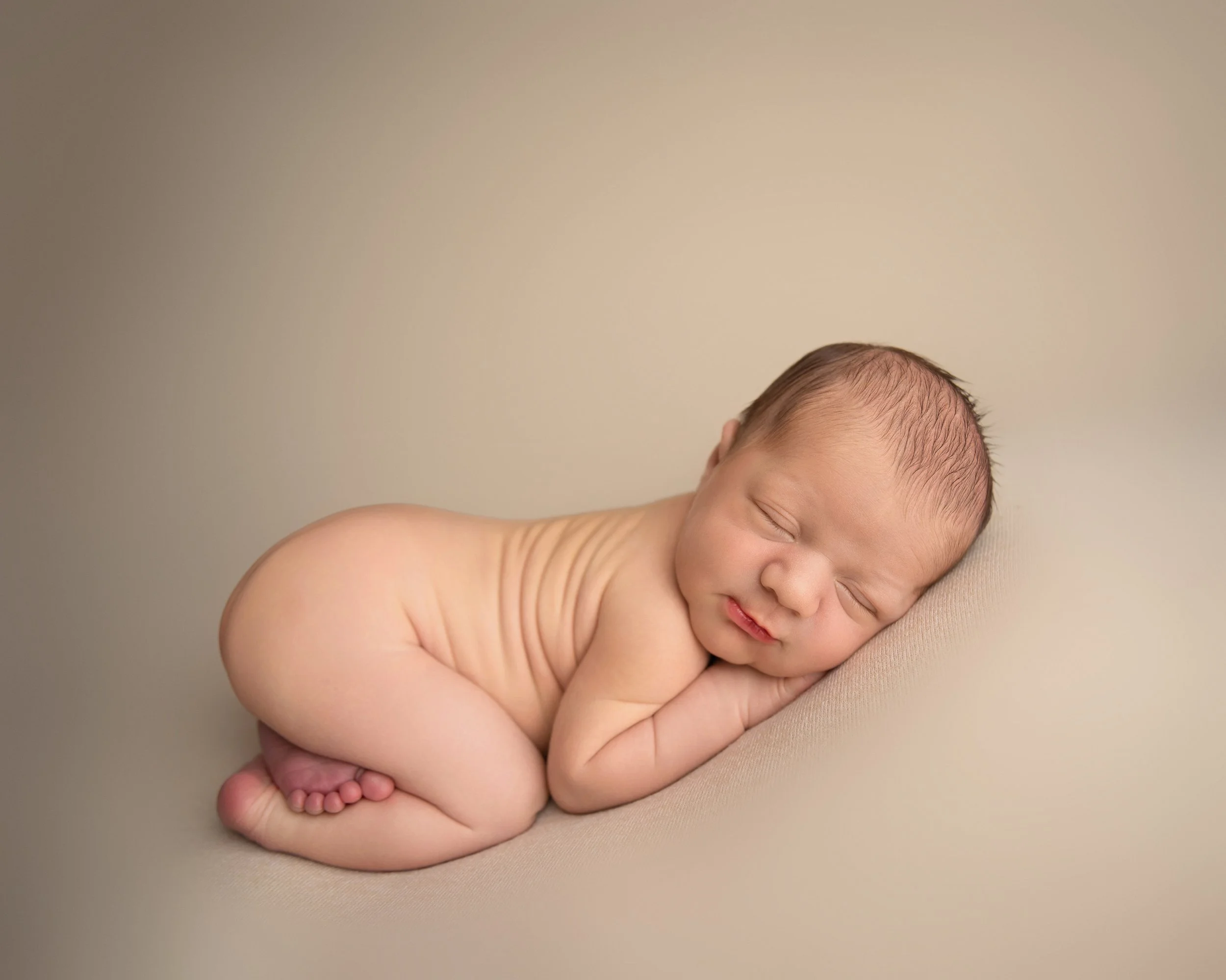 A sleeping newborn baby lying on its side on a beige surface.