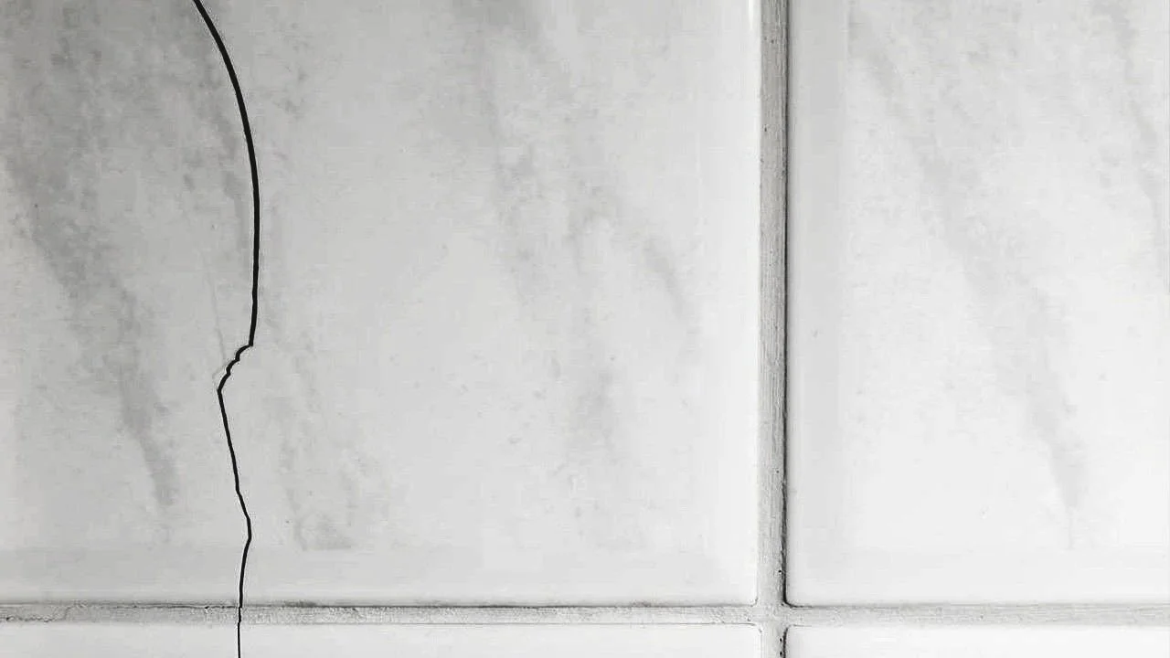 Close-up of a crack running through the white tiles on a wall.