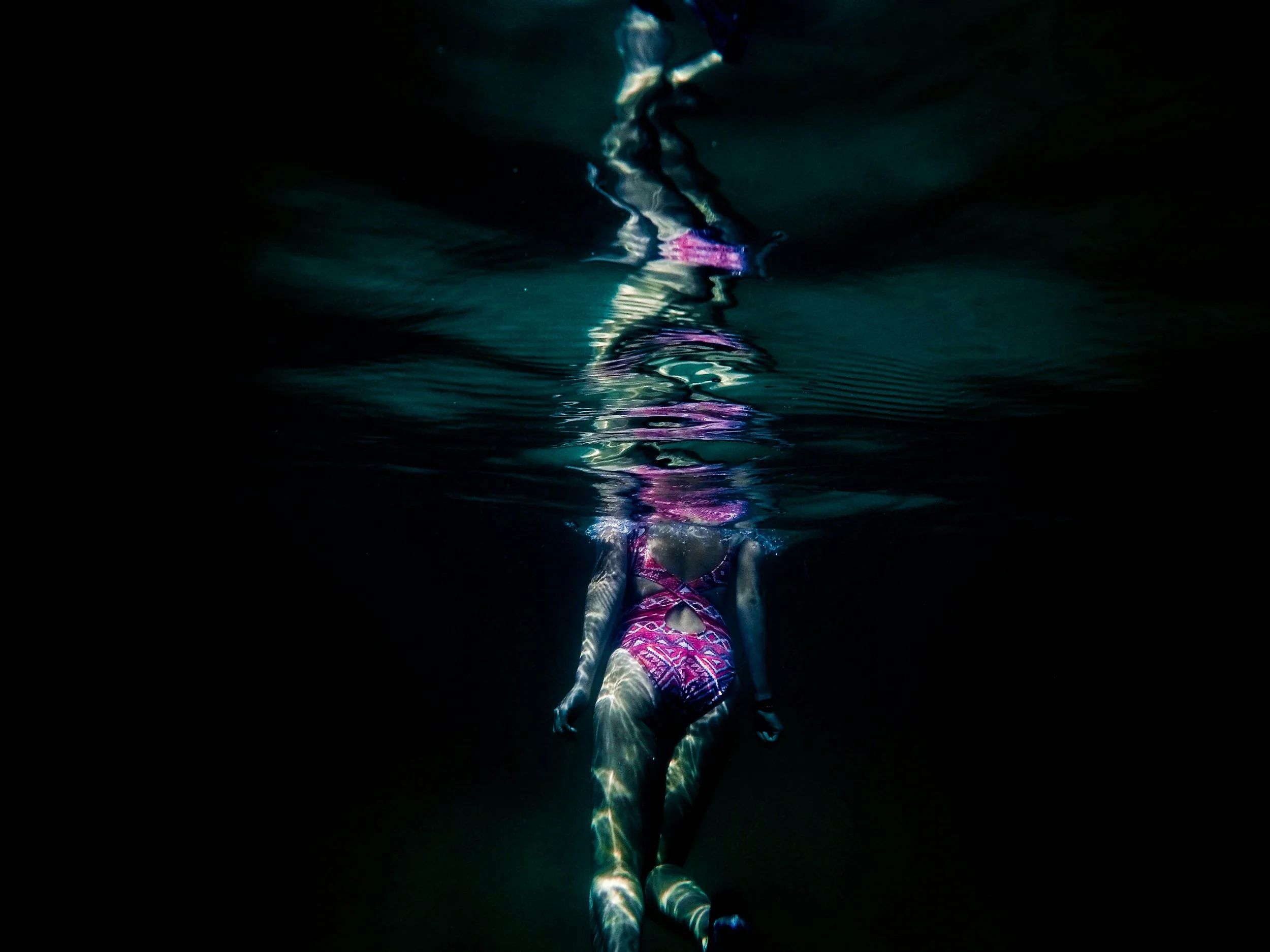 A person swimming underwater wearing a purple and pink patterned swimsuit.