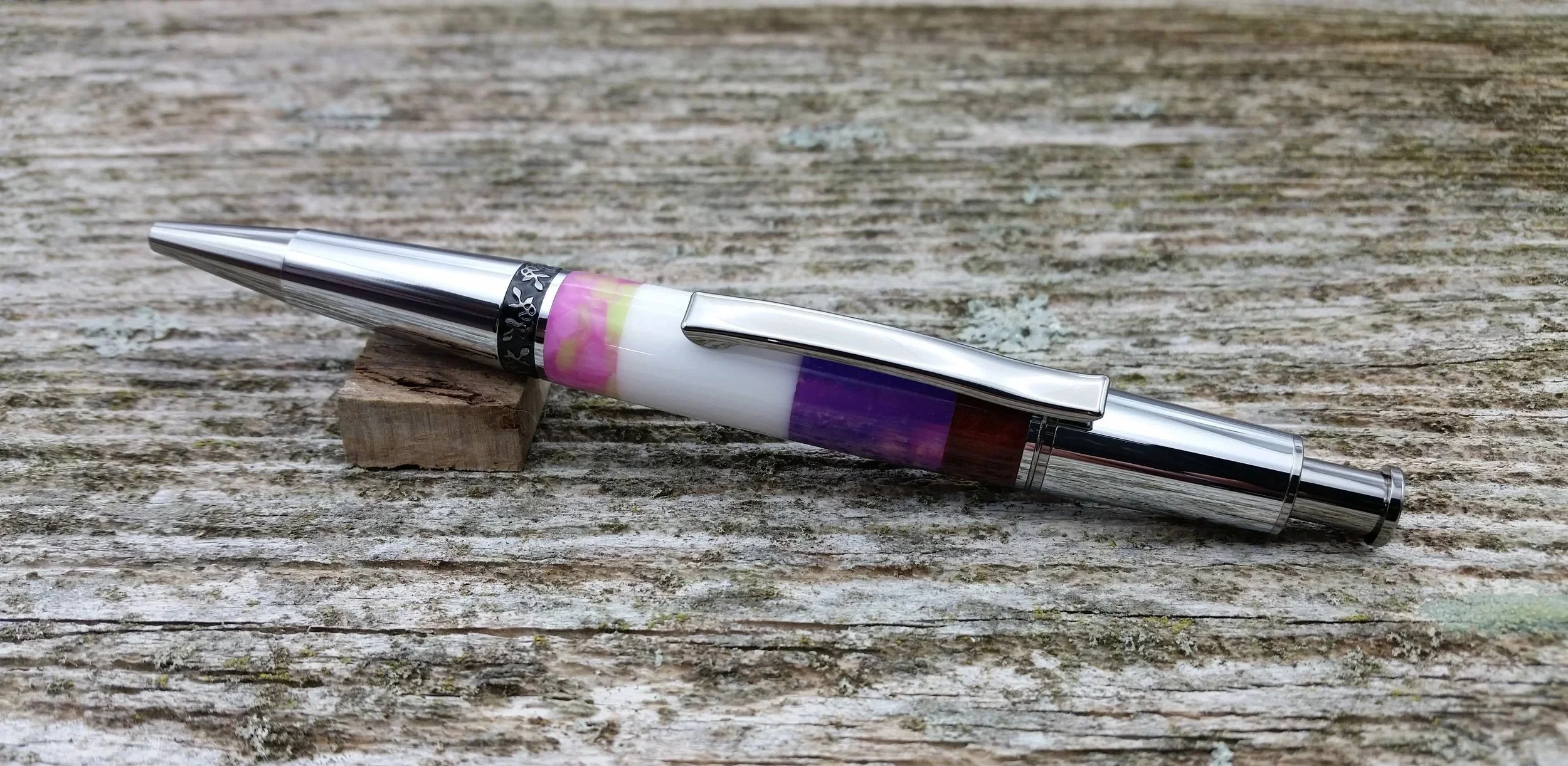 A silver and multicolored ballpoint click pen resting on a weathered wooden surface.