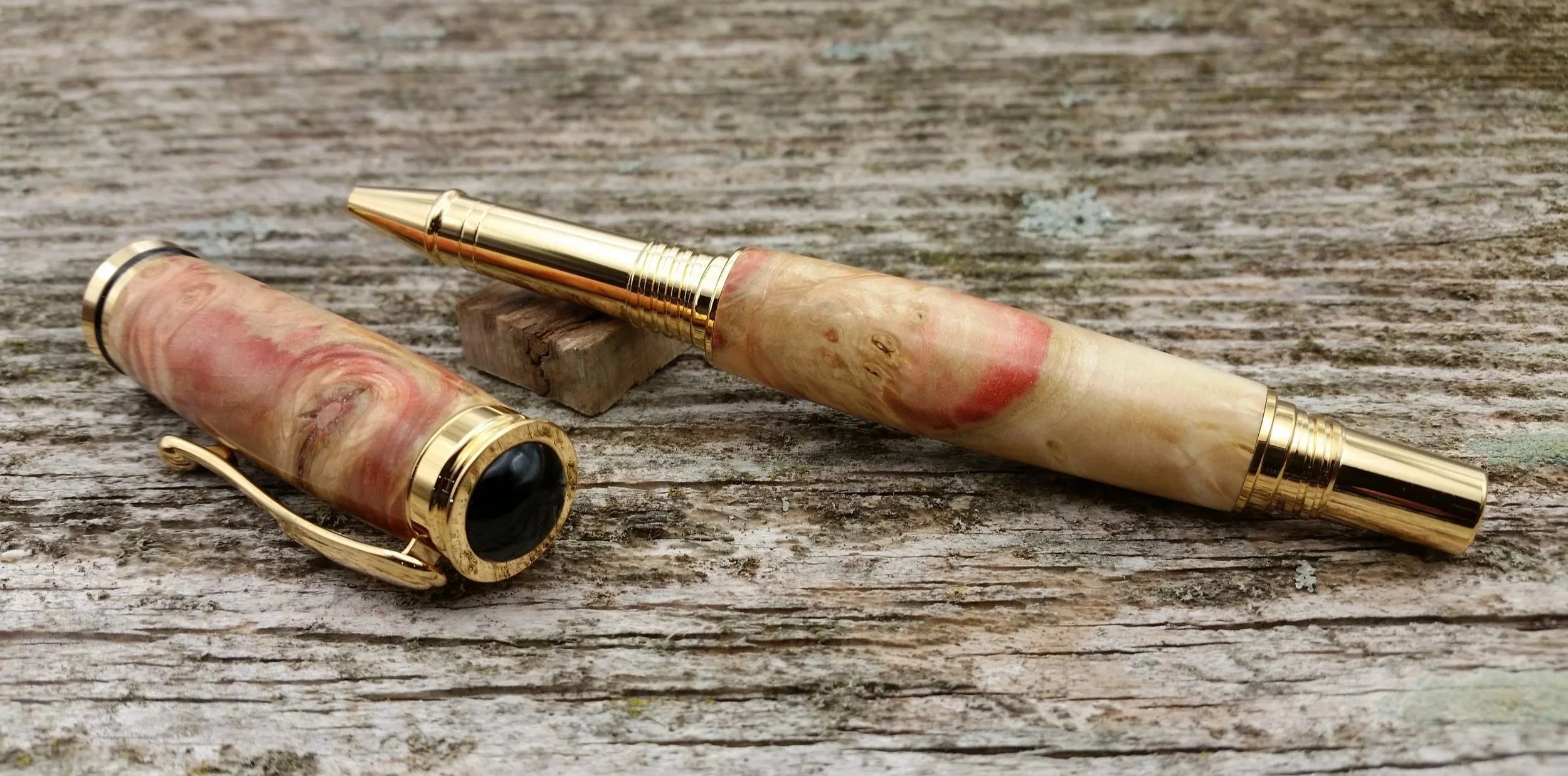 Parus Pen retro style rollerball pen with gold accents and a marbled pink, beige, and red body, resting on a weathered wooden surface.
