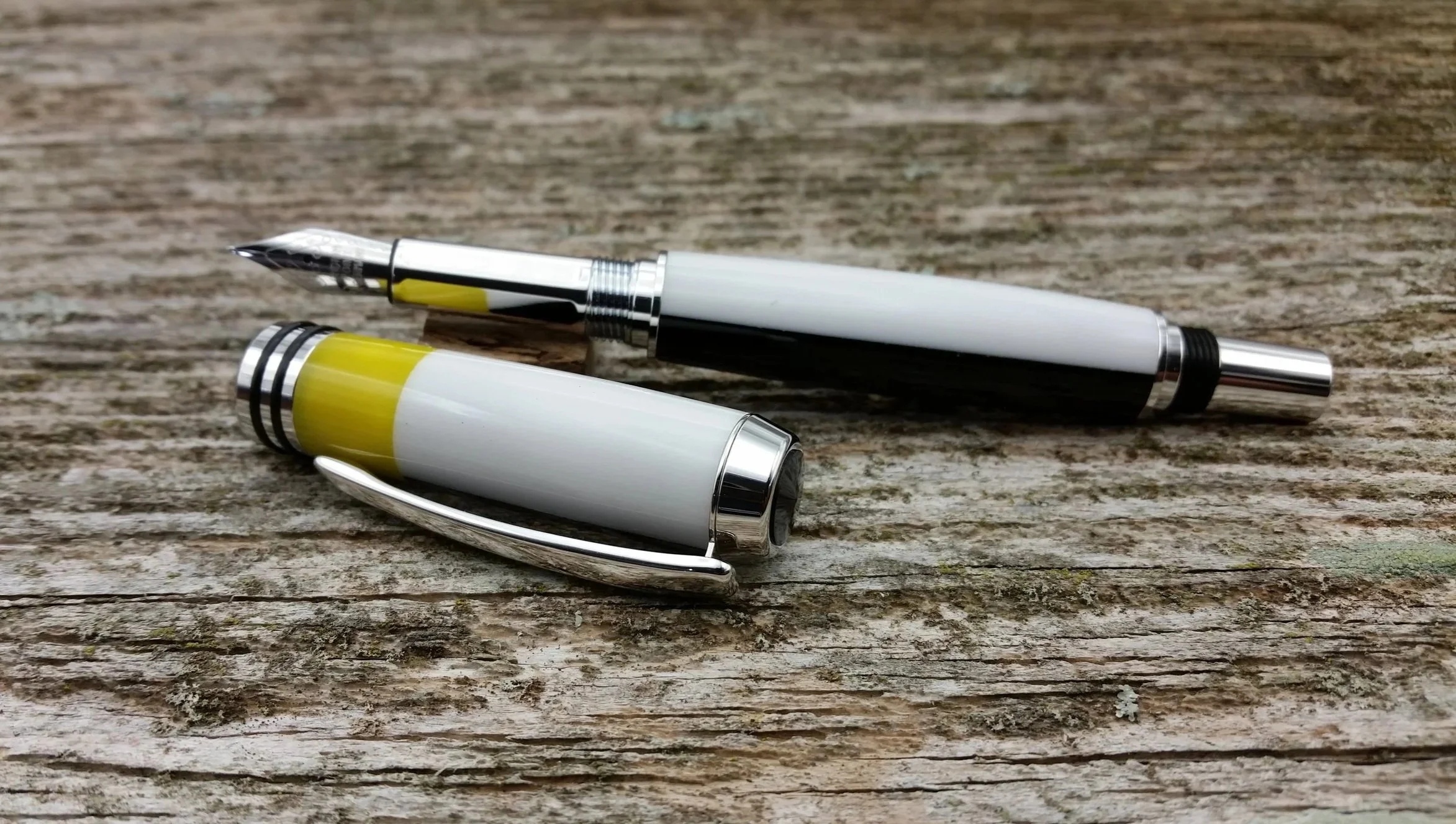 Parus Pen white, yellow, and black fountain pen with silver accents resting on a weathered wooden surface.