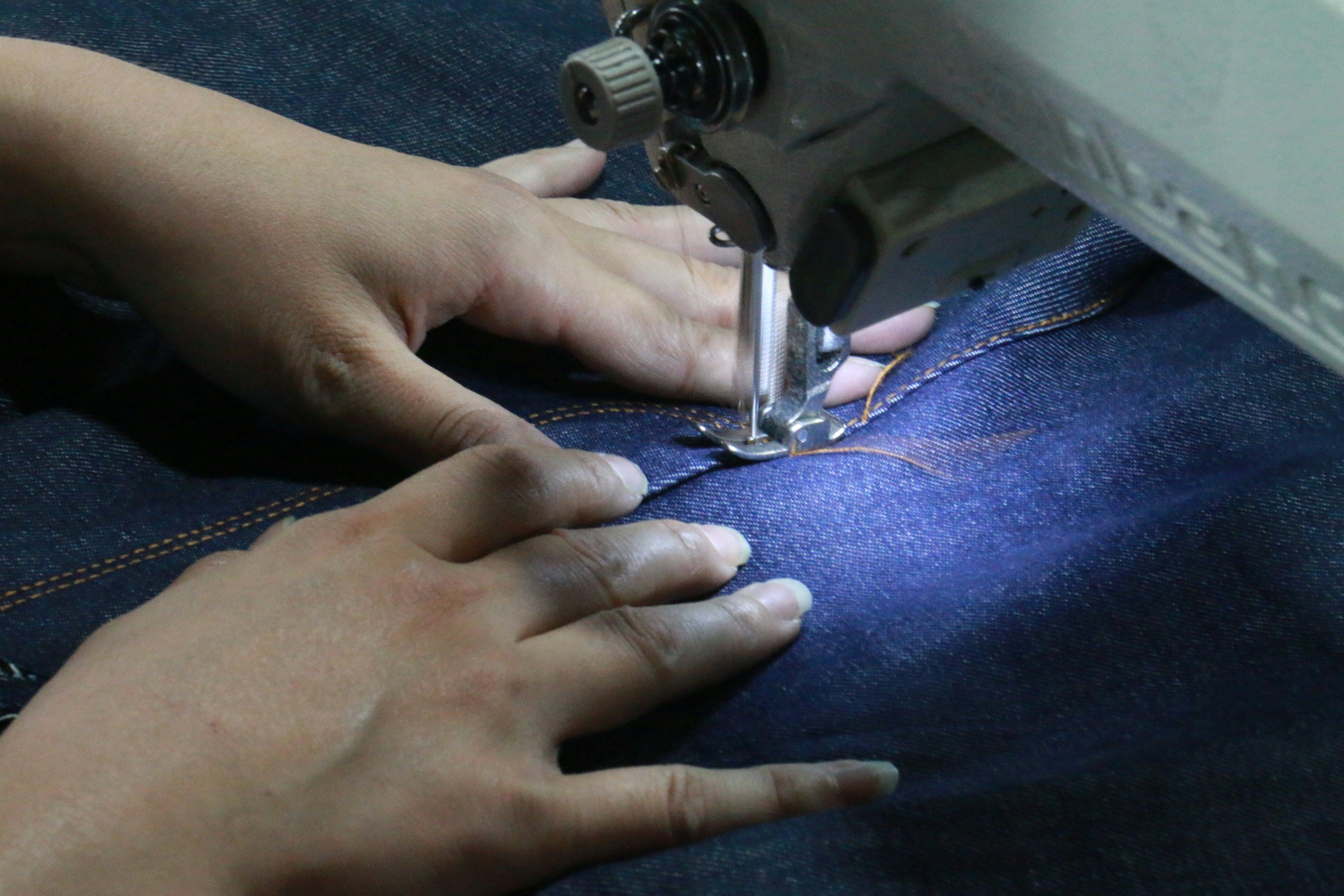 Close-up of hands guiding denim fabric through a sewing machine as it stitches a seam.