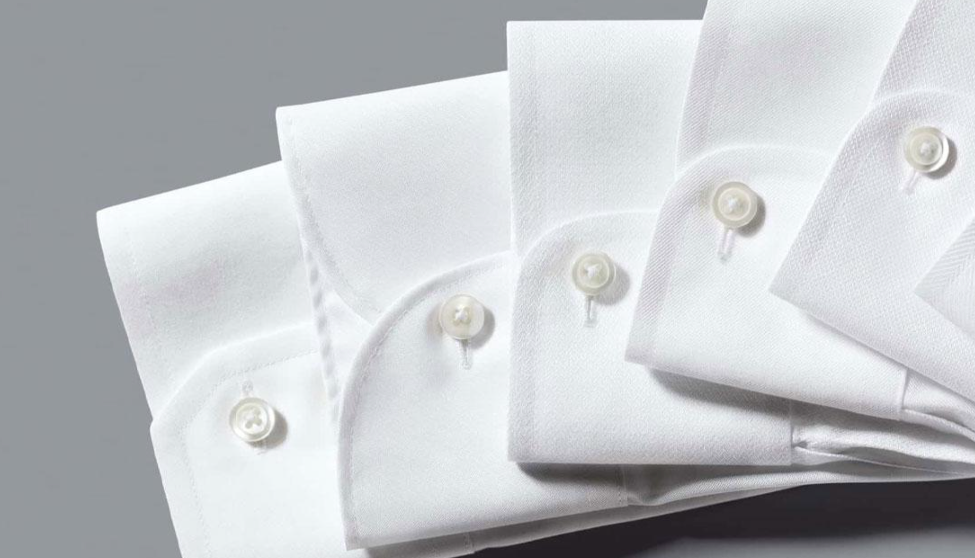 Close-up of a white dress shirt collar and cuffs with pearl buttons on a grey background.